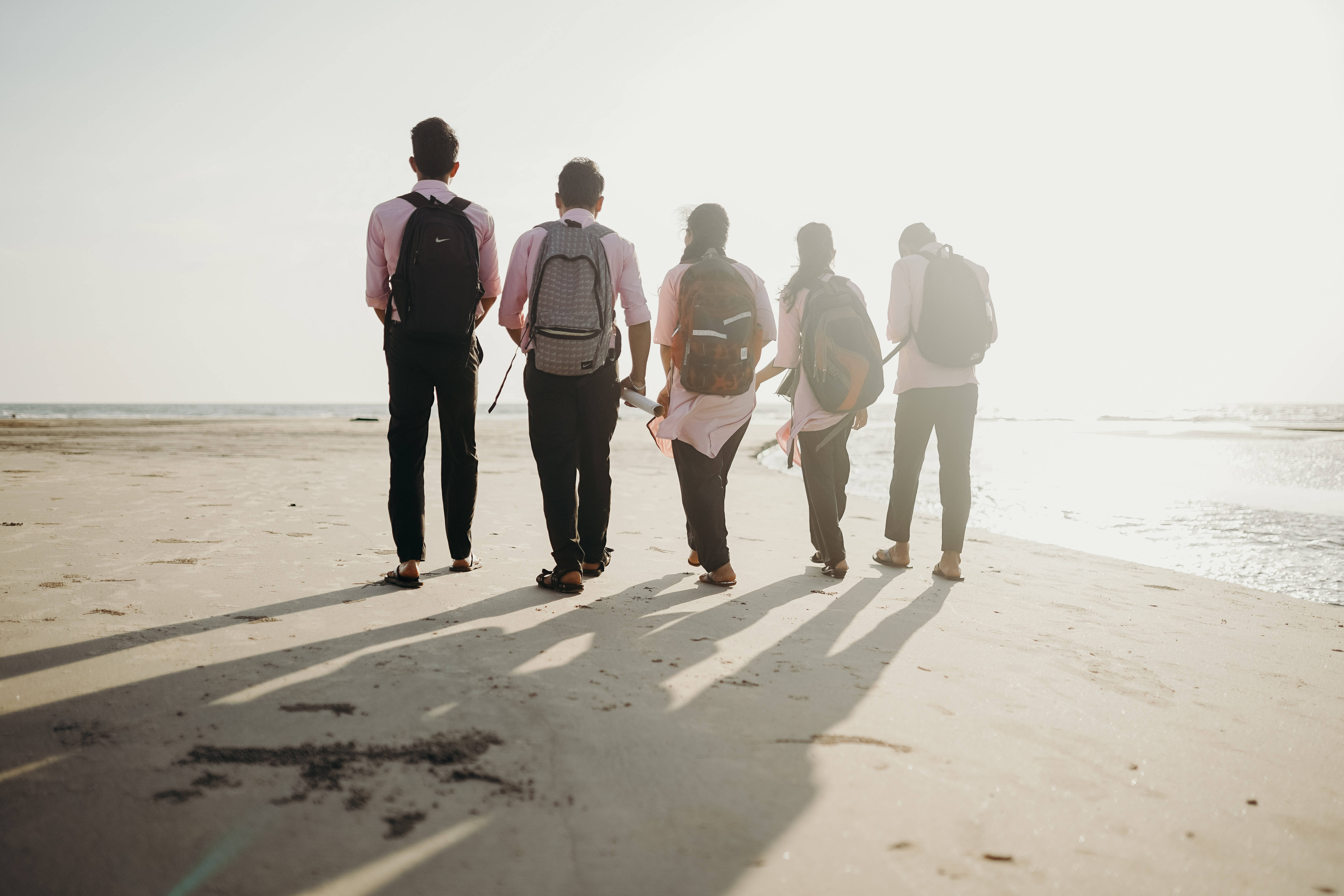 Friendship 桌布 壁紙 — 五個背著背包的朋友在陽光明媚的海灘上走遠，向海洋地平線投下長長的影子。