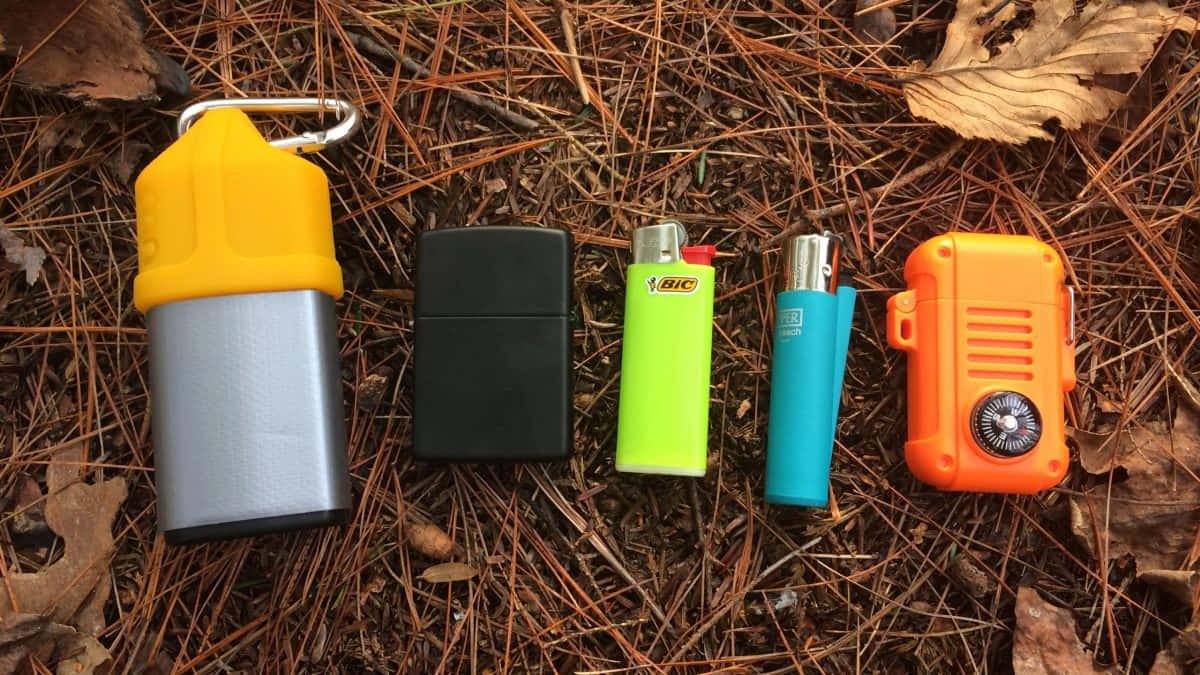 lighter 桌布 壁紙 — 五個色彩繽紛的打火機和一個指南針盒放在松針和枯葉上。