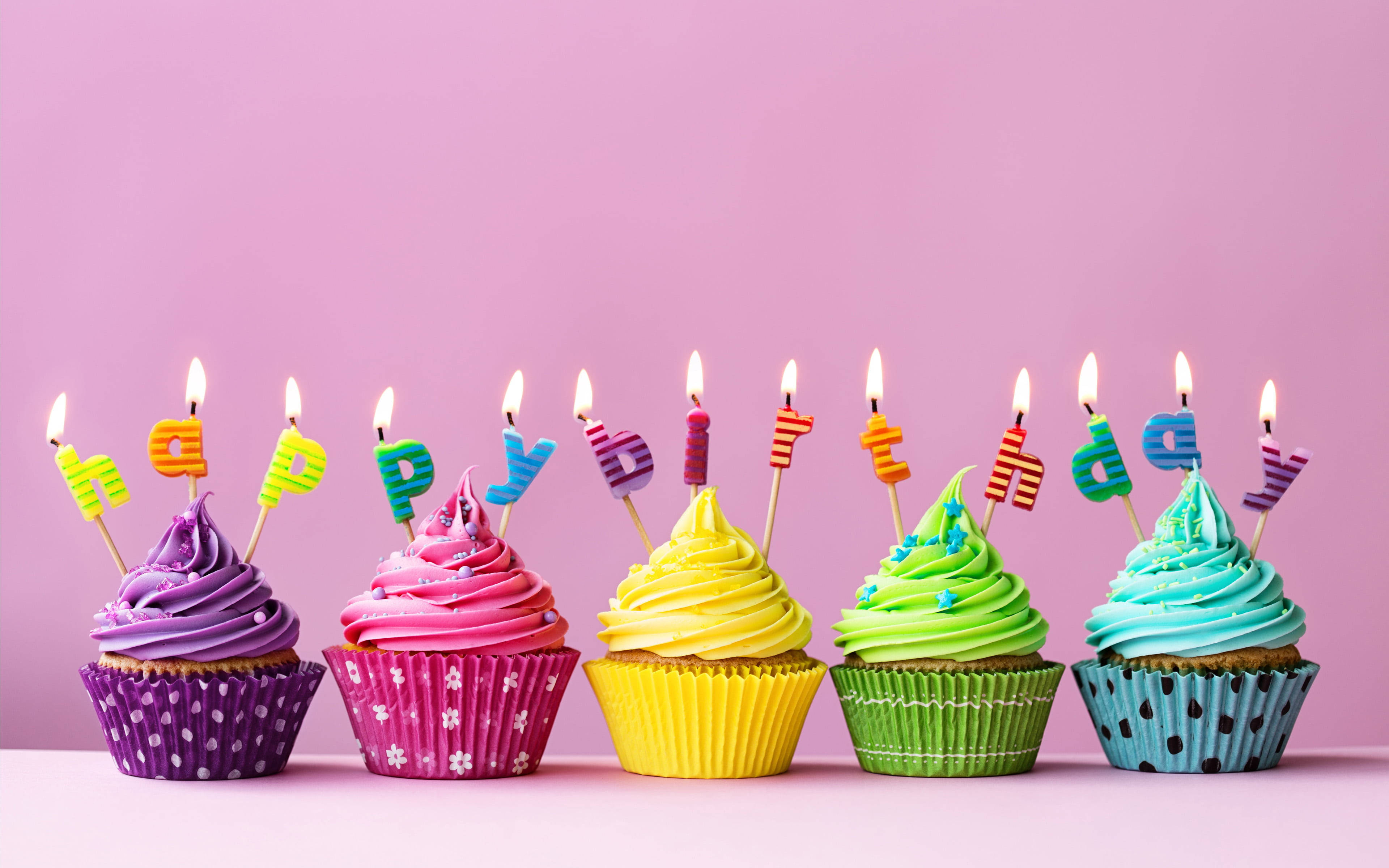 my 桌布 壁紙 — 五個色彩繽紛的杯子蛋糕，上面有燃燒的蠟燭拼出 happy birthday，背景是柔和的粉紅色。