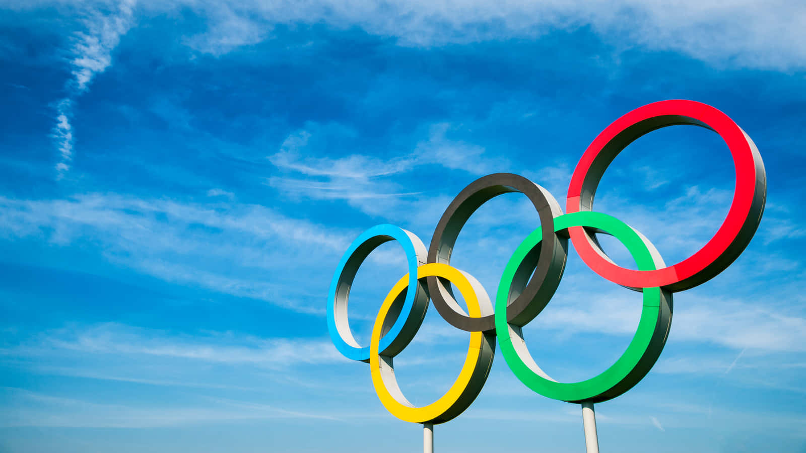 奧運 桌布 壁紙 — 五個色彩鮮豔、環環相扣的奧運五環，在藍天白雲的映襯下高高聳立。