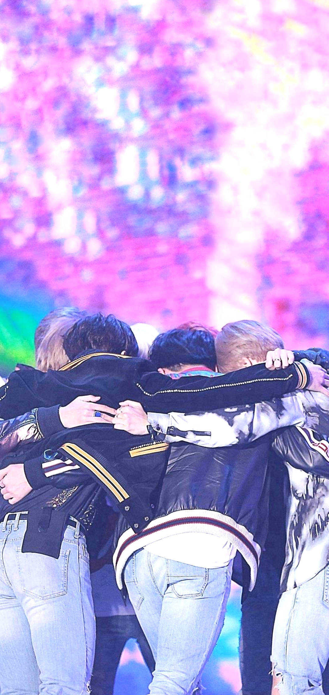 BTS 鎖定螢幕 桌布 壁紙 — 五個身穿外套的年輕男子擠在一個燈光璀璨的舞台上，身後是充滿活力的粉紅色和紫色燈光。