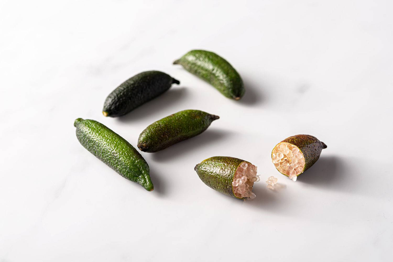 Fruits 桌布 壁紙 — 五個金桔放在白色大理石表面上，其中一個切開，露出半透明的粉紅色果肉。