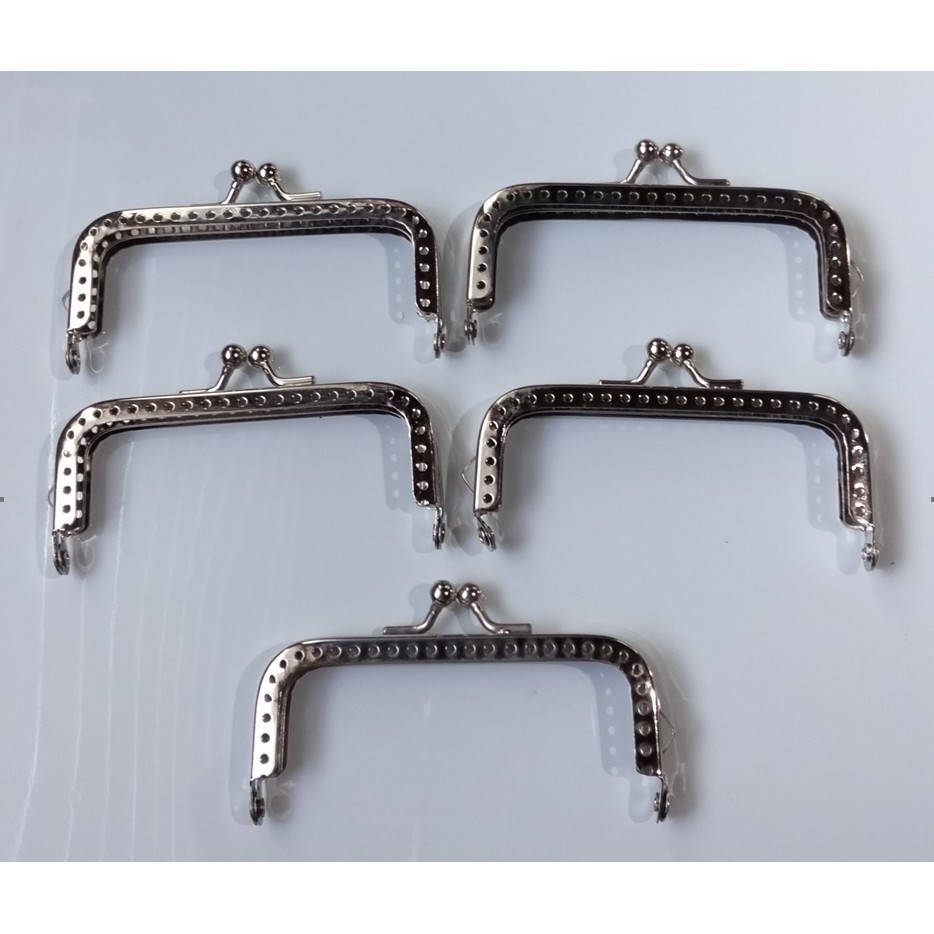 Material 桌布 壁紙 — 五個銀色金屬錢包扣，帶有圓點邊緣，整齊排列在純白色表面上。