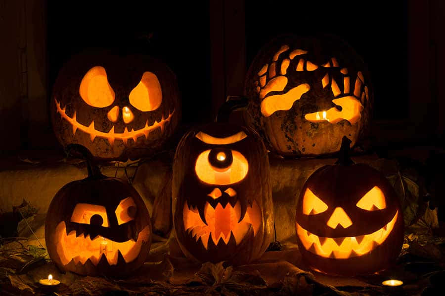 Jack O Lantern 桌布 壁紙 — 五個雕刻精細、發光的傑克南瓜燈，帶著兇惡的面孔，照亮了黑暗的萬聖節夜晚場景。