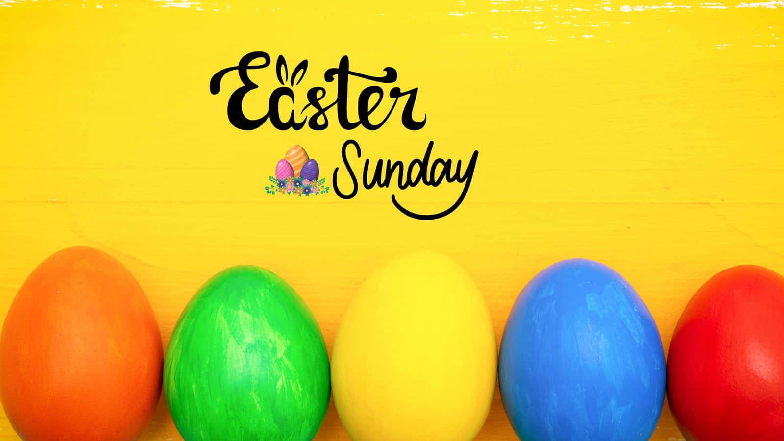 Easter Zoom 桌布 壁紙 — 五個鮮豔彩繪的復活節蛋，顏色為橙色、綠色、黃色、藍色和紅色，放在一個明亮的黃色木質表面上，下方有文字「復活節星期日」。