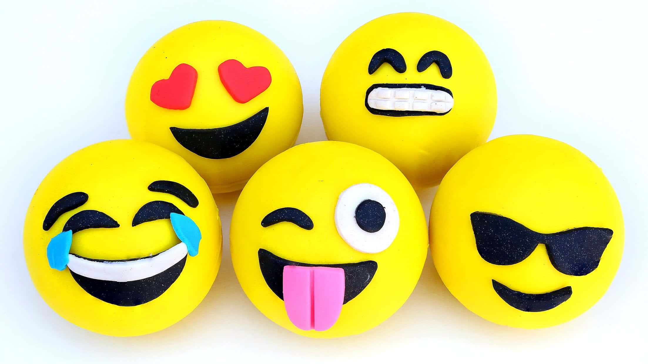 Smile 桌布 壁紙 — 五個鮮黃色表情符號形狀的翻糖蛋糕，帶有俏皮的表情，如心形眼睛和伸出舌頭。