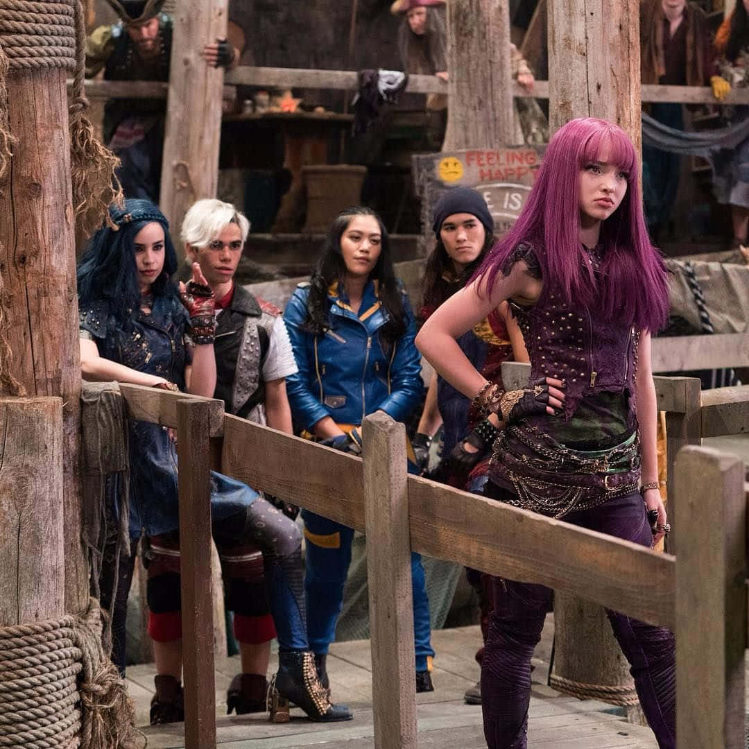 Disney Descendants 桌布 壁紙 — 五名年輕叛逆者，擁有鮮豔的髮色和時尚前衛的服裝，挑釁地站在一個質樸西部小鎮的木製碼頭上。