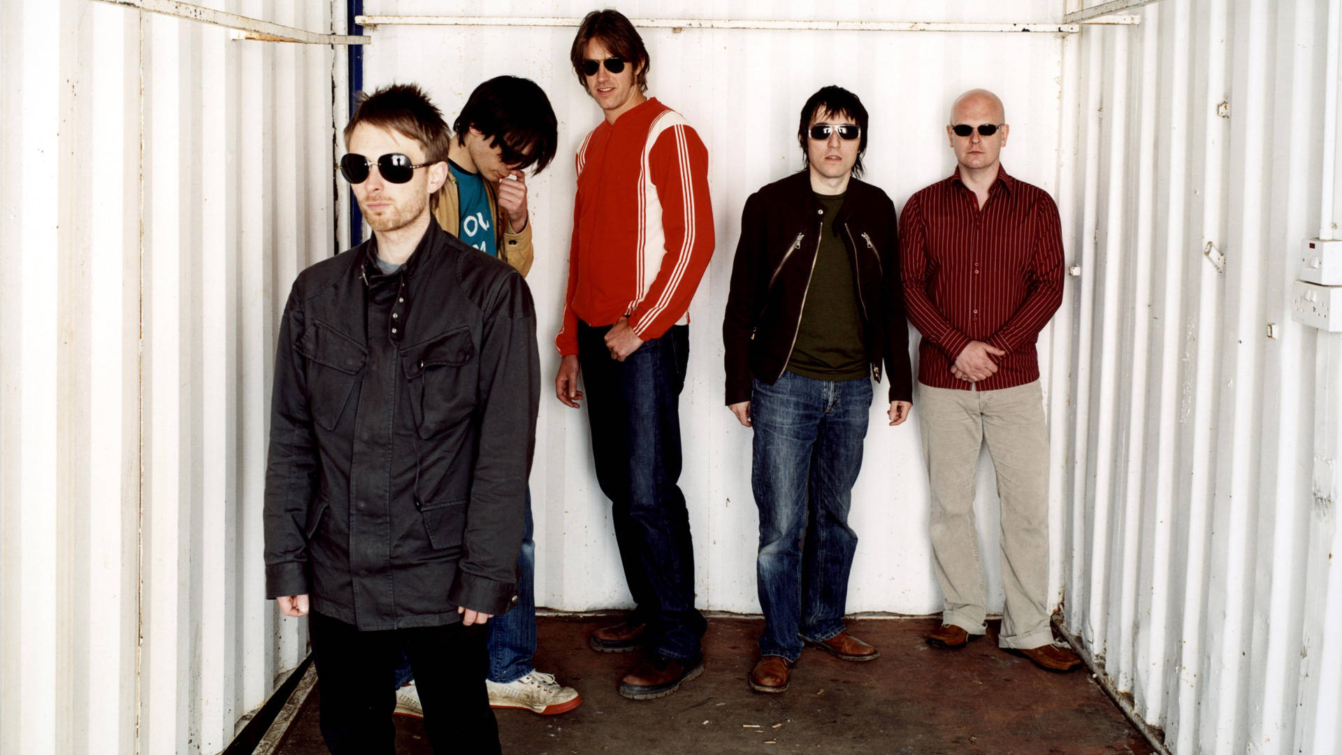 band 桌布 壁紙 — 五名戴著太陽眼鏡、穿著休閒服裝的男子自信地站在白色貨櫃內。