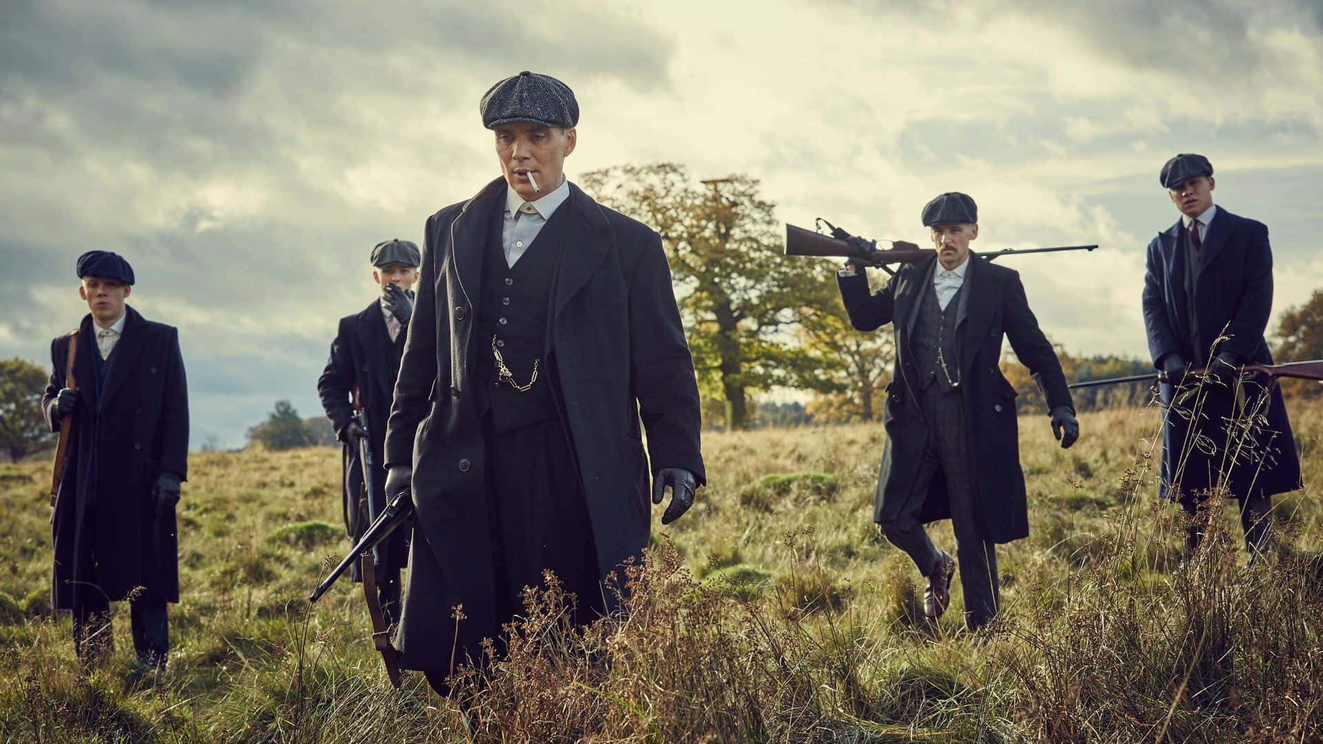 五名身穿復古服裝、手持步槍的男子走過草地。 — Peaky Blinders 壁紙