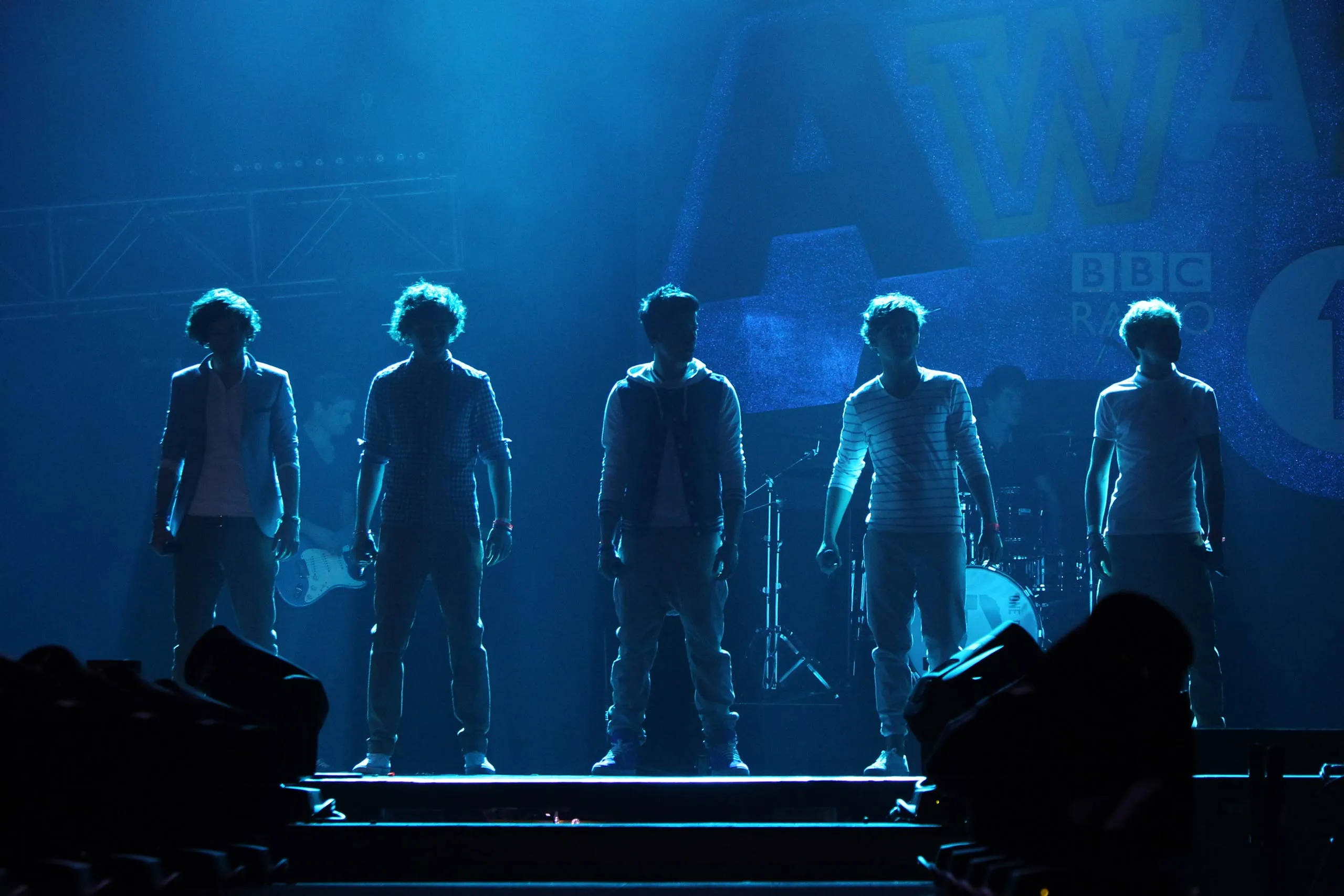 One Direction Aesthetic 桌布 壁紙 — 五名樂團成員以剪影姿態站在一個沐浴在強烈藍光中的舞台上，背後可見BBC Radio 1標誌。