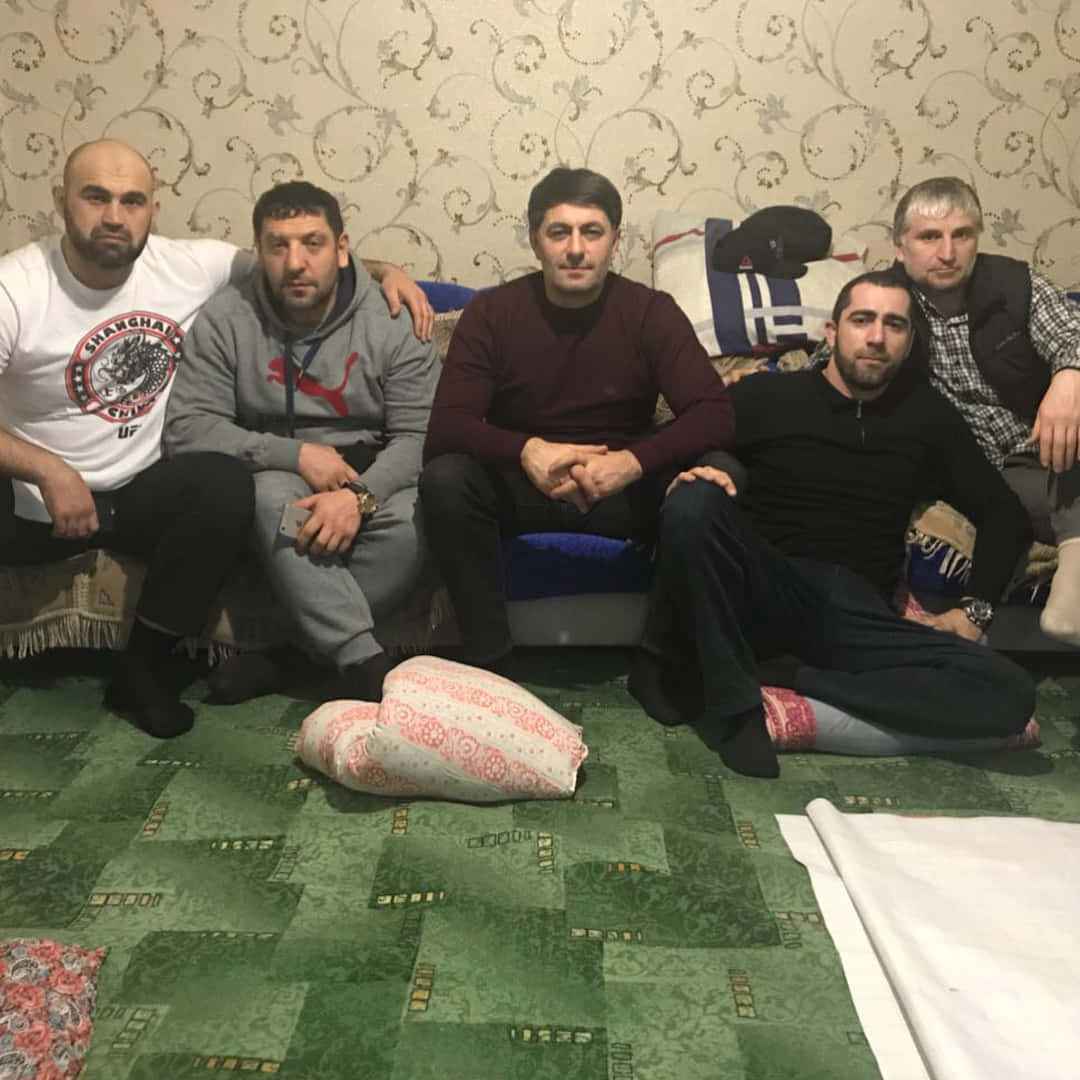 MMA 桌布 壁紙 — 五名男子在舒適的室內環境中，坐在有圖案的綠色地毯上，背景是華麗的壁紙。