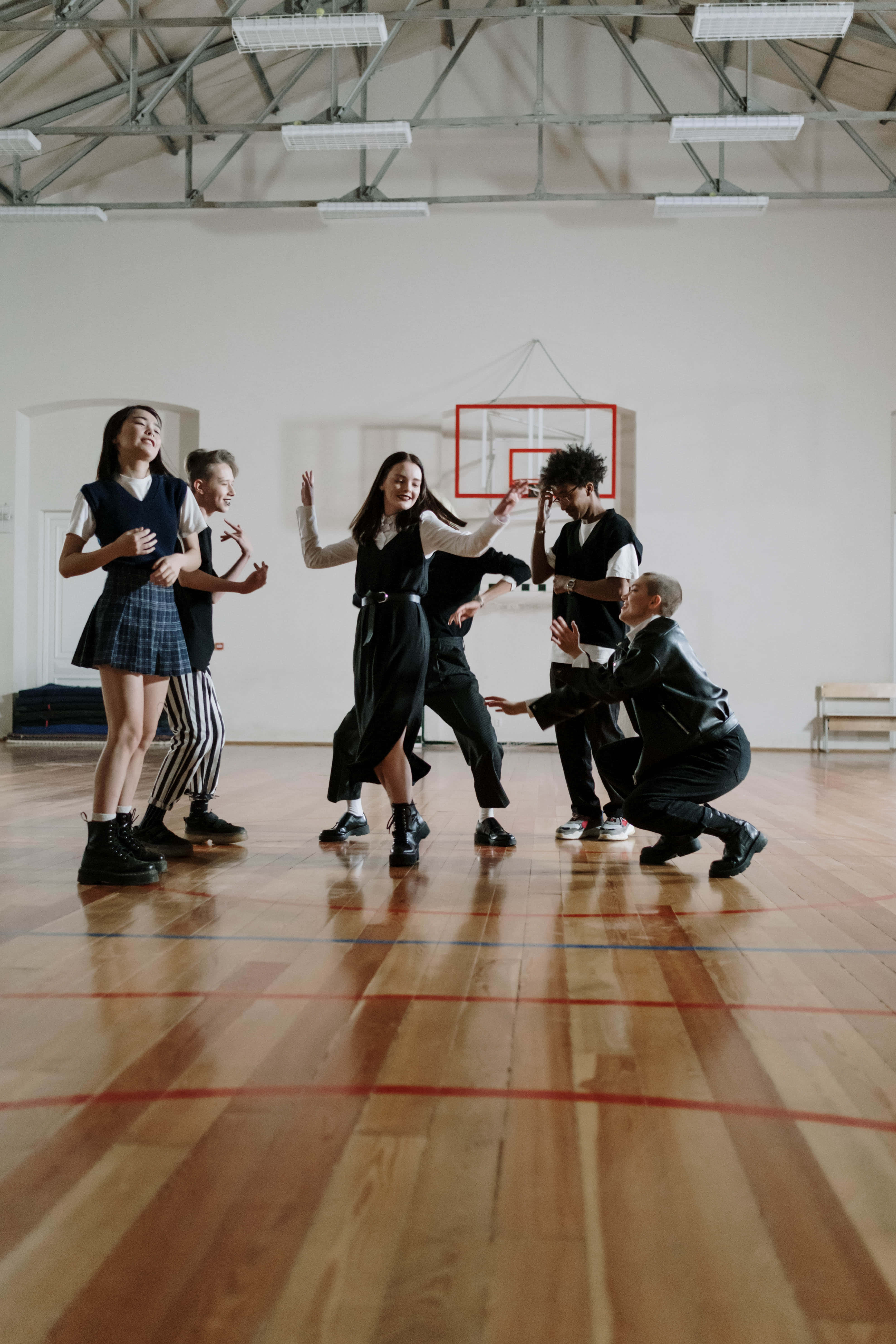 Physical Education 桌布 壁紙 — 五名身穿校服的年輕人在明亮的螢光燈下，在木製體育館地板上充滿活力地跳舞。