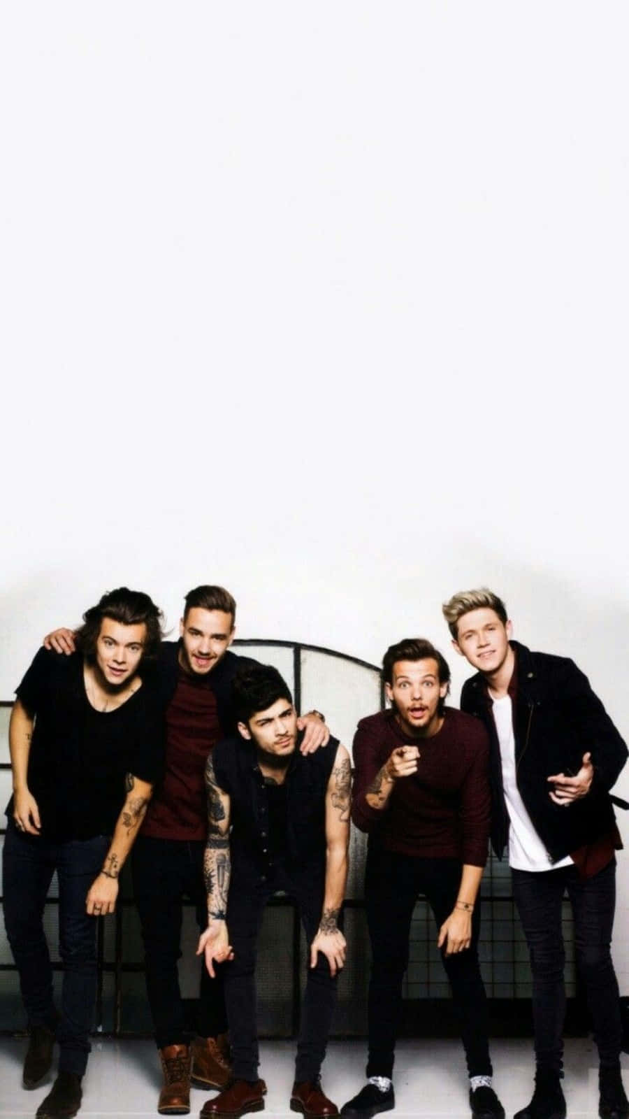 1 Direction iPhone 桌布 壁紙 — 五名身穿深色休閒服的年輕男子在一個純白色牆壁前擺出俏皮的姿勢，身後有金屬欄杆。