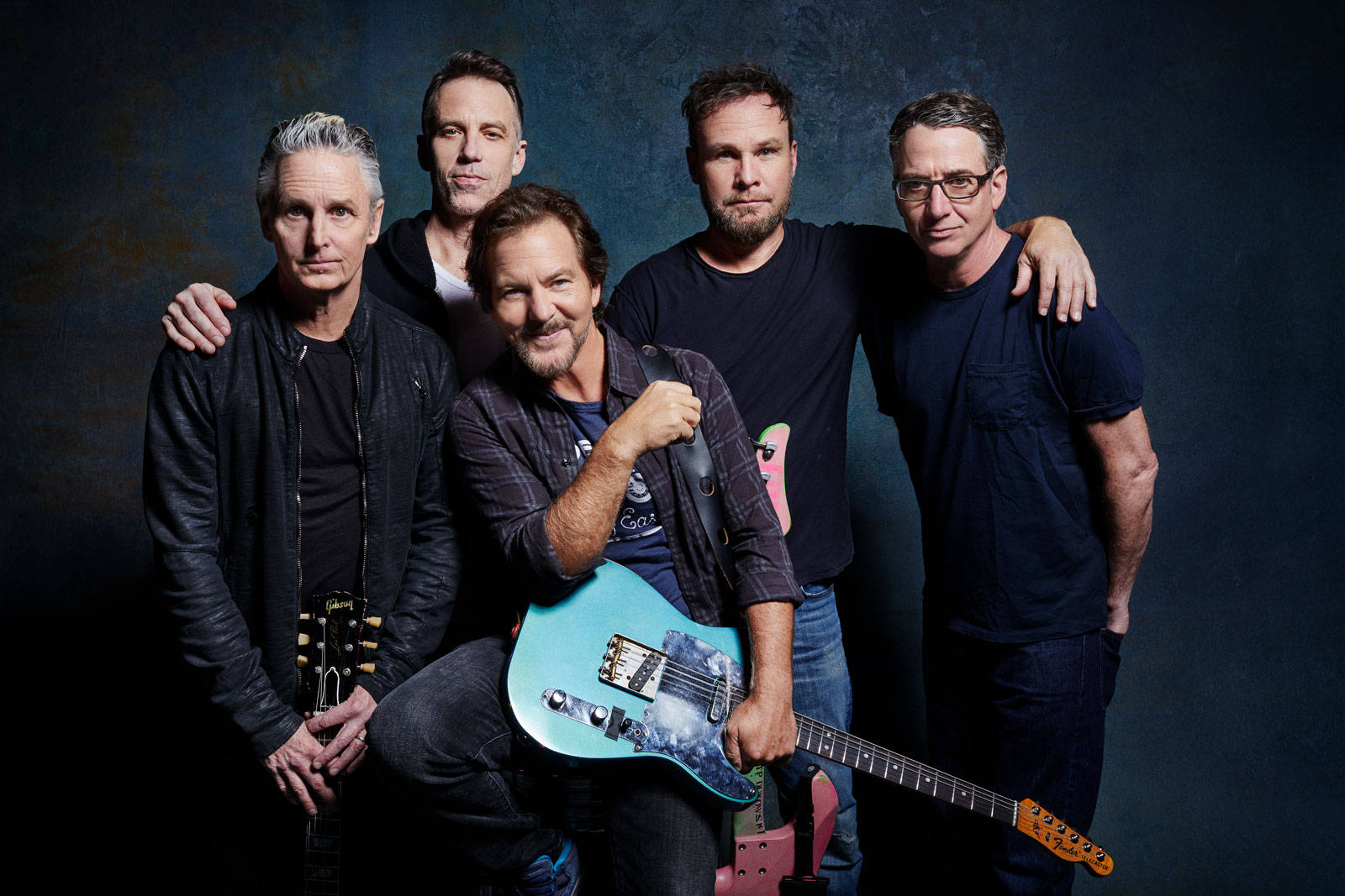pearl jam 桌布 壁紙 — 五名身穿深色衣服的男子在帶有紋理的深藍色工作室背景前緊密地擺姿勢，手持吉他。