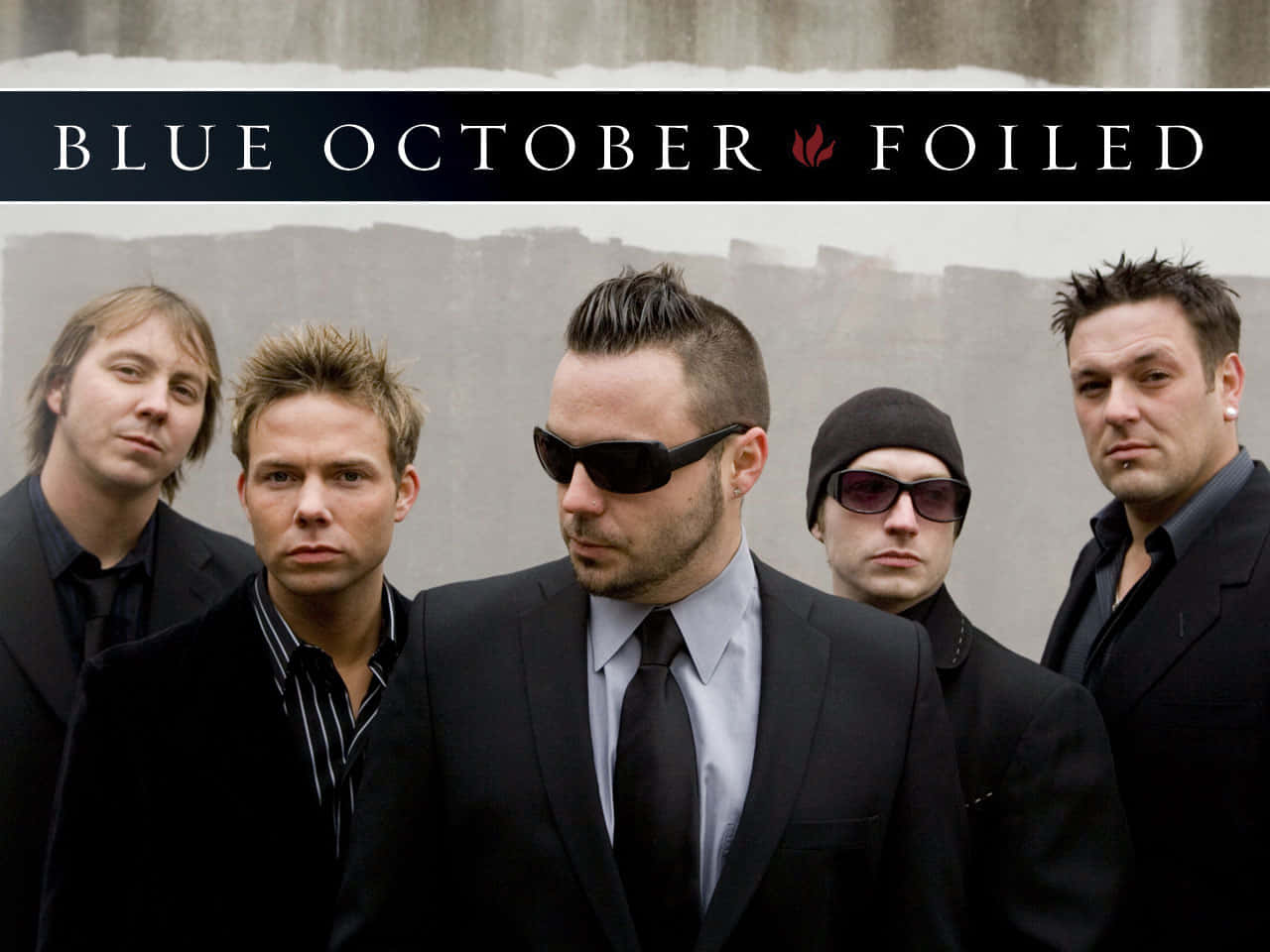 Blue October 桌布 壁紙 — 五名身穿深色西裝和太陽眼鏡的男子，在寫有「BLUE OCTOBER FOILED」的橫幅下，莊嚴地站在有紋理的灰色牆壁前。