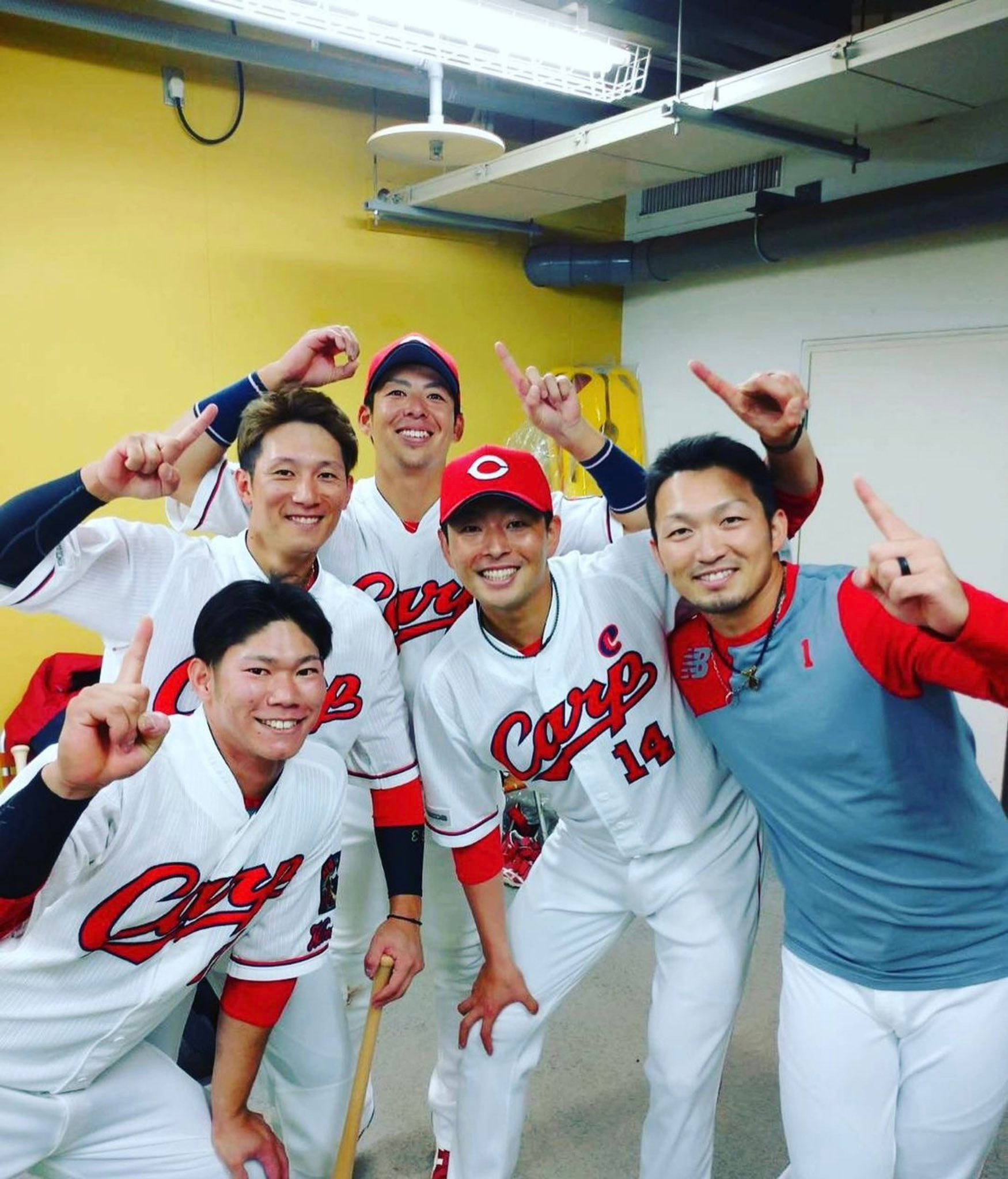 運動 桌布 壁紙 — 五名身穿白色 Carp 球衣的棒球運動員面帶微笑，在黃色牆壁和暴露天花管道的休息區愉快地擺姿勢。