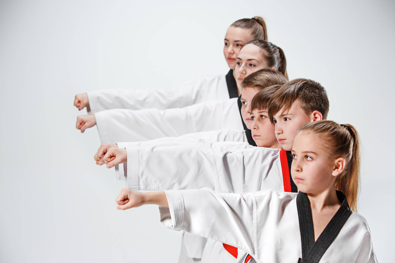 martial arts 桌布 壁紙 — 五名身穿白色空手道服、繫著黑帶的兒童，在純白背景前站成斜線，雙臂向前伸展，做出同步的武術姿勢。