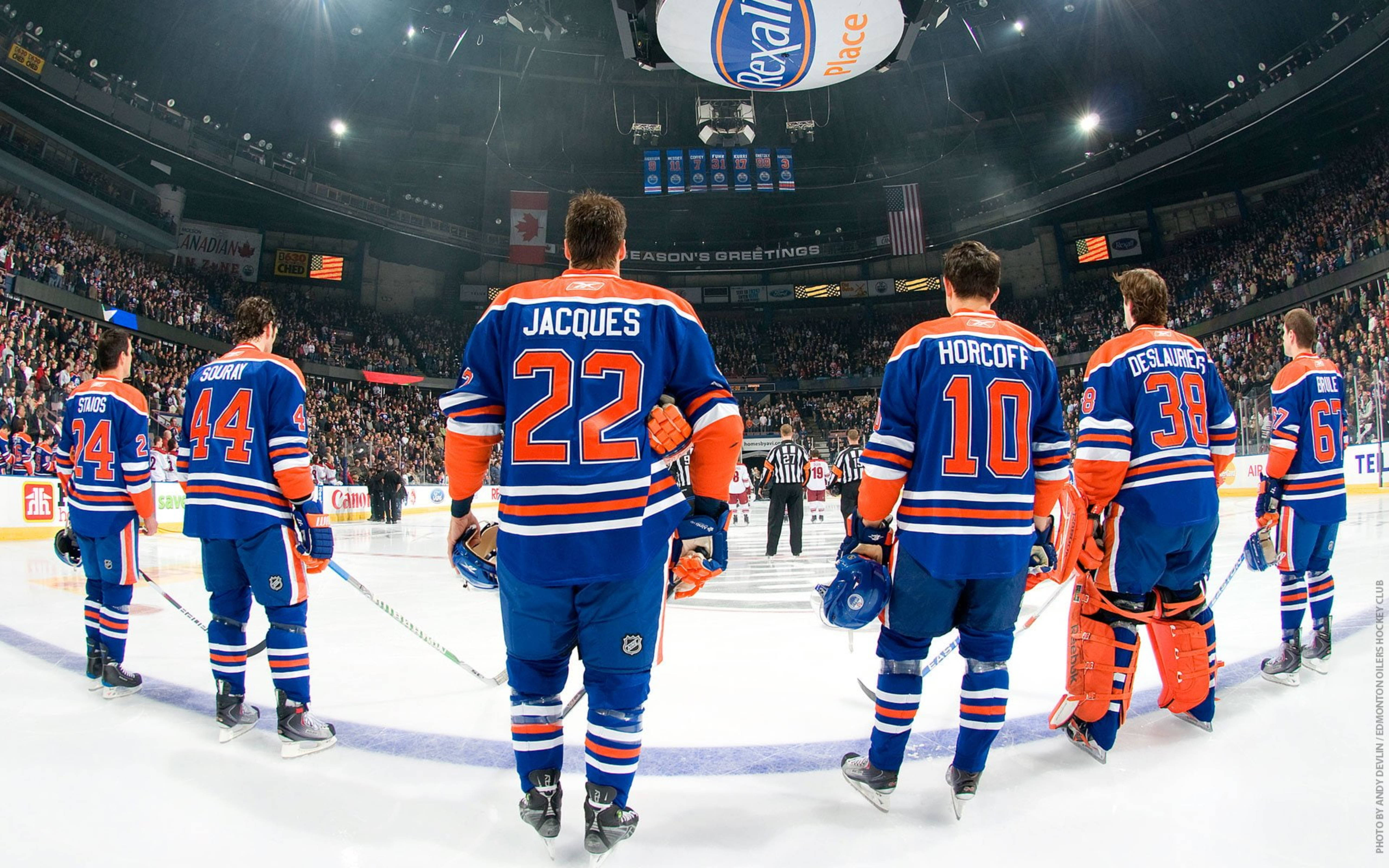 Oilers 桌布 壁紙 — 五名身穿藍色和橙色球衣的愛德蒙頓油人冰球球員在冰上背對鏡頭走開，身後是座無虛席的場館。