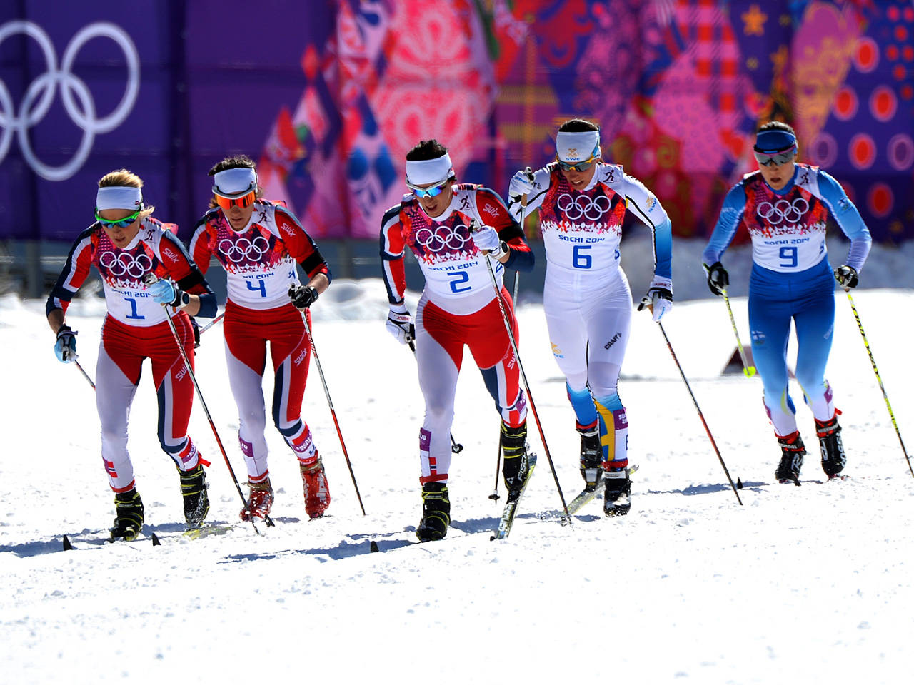 運動 桌布 壁紙 — 五名身穿鮮豔紅、白、藍色制服的女越野滑雪選手，在明亮的日光下於雪道上激烈競賽。