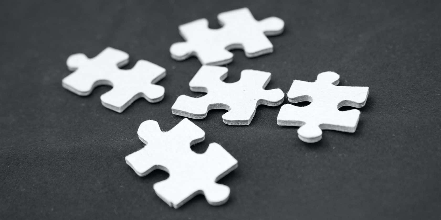 Puzzle 桌布 壁紙 — 五塊白色拼圖碎片散落在帶有柔和陰影的深色紋理表面上。