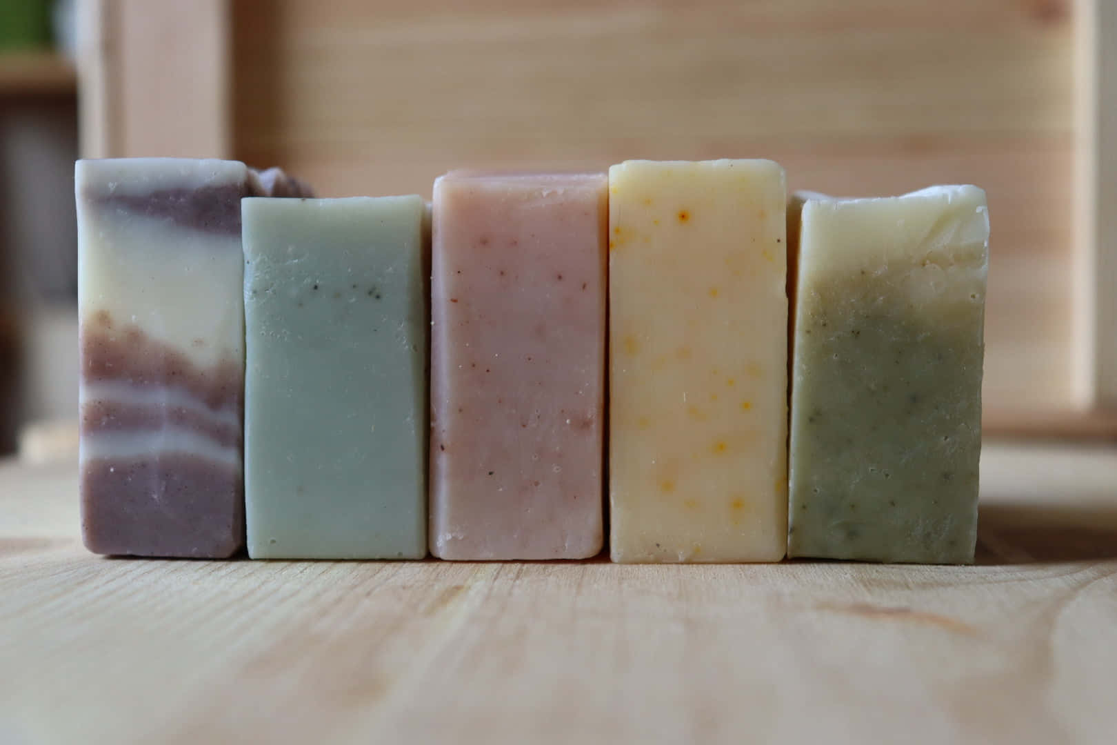 bath 桌布 壁紙 — 五塊粉彩色調的手工皂整齊排列在淺色木質表面上，伴隨著柔和自然光線。