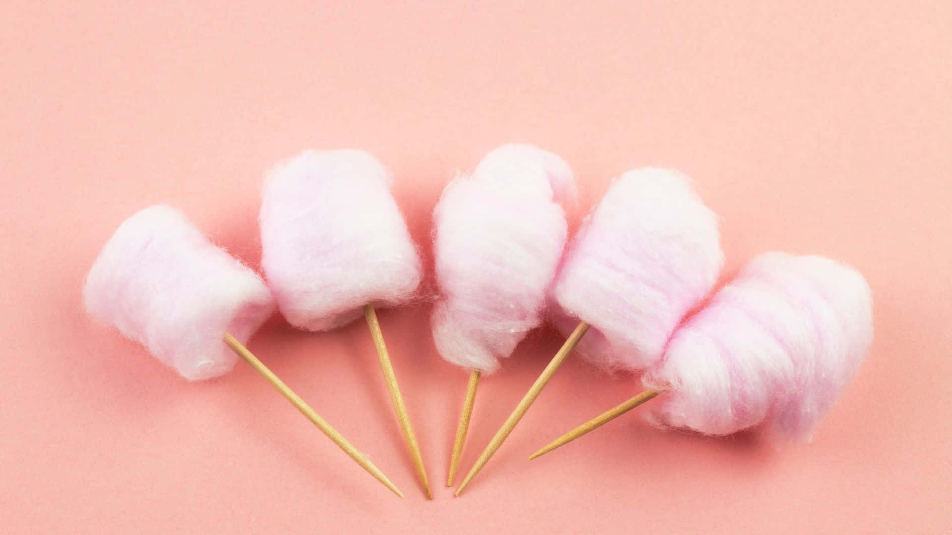 Cotton Candy 桌布 壁紙 — 五塊蓬鬆粉紅棉花糖插在木棒上，以扇形排列在柔和粉紅背景前。