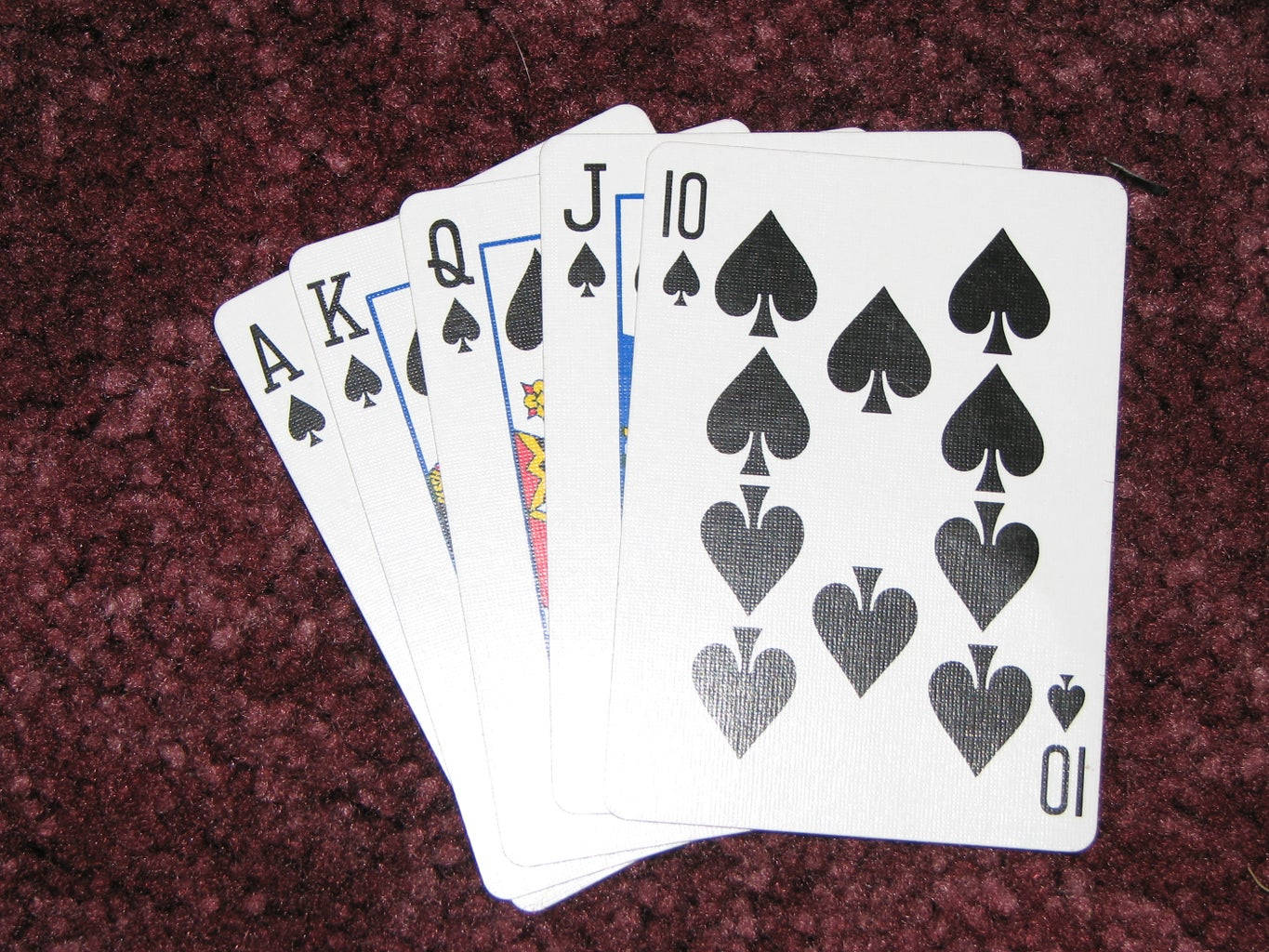 Poker 桌布 壁紙 — 五張黑桃撲克牌扇形展開在深紅色有紋理的地毯上，顯示A、K、Q、J及10。