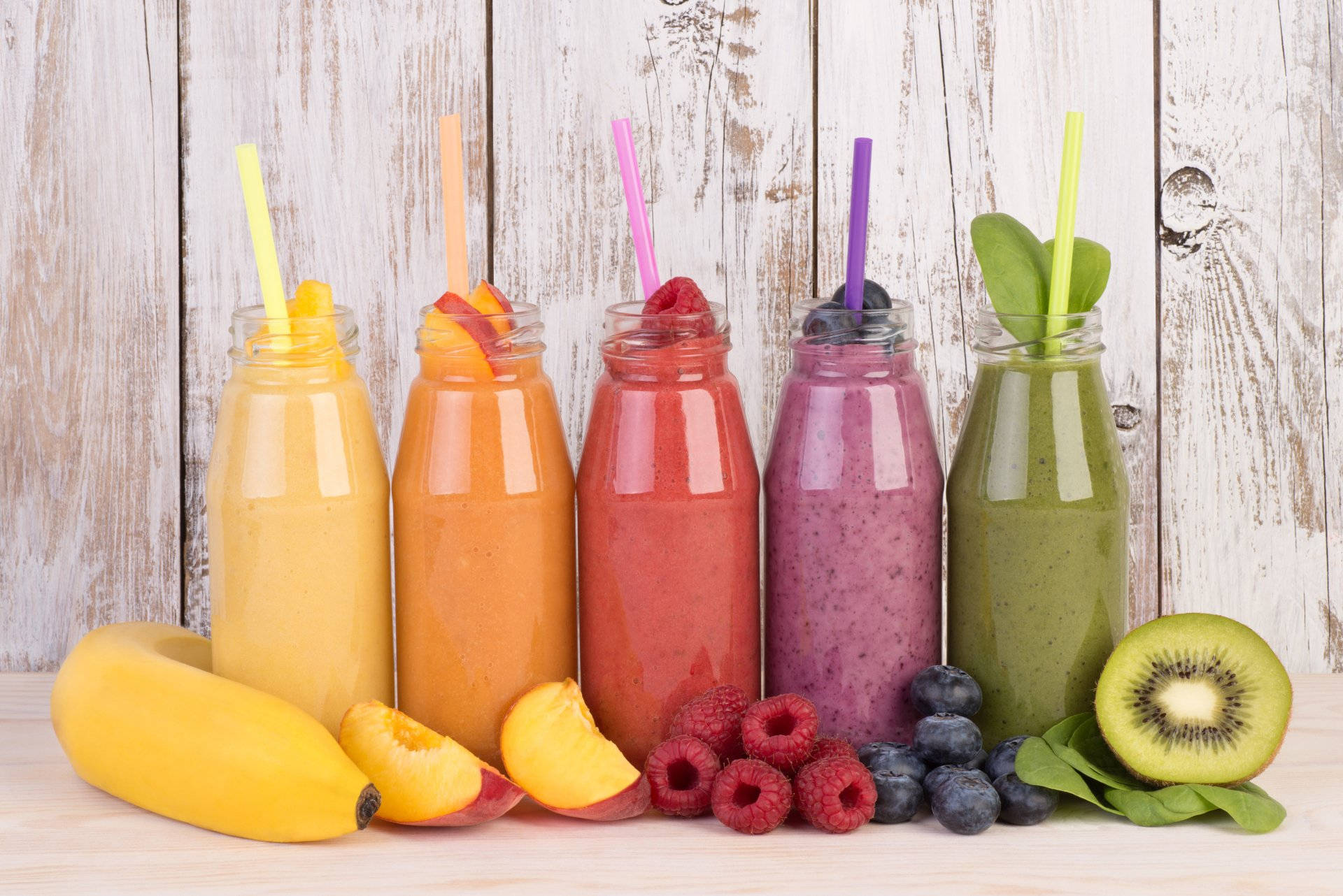 Smoothie 桌布 壁紙 — 五杯色彩繽紛的冰沙裝在玻璃瓶中，附有吸管，旁邊放著新鮮水果，置於經風化的木質表面上。