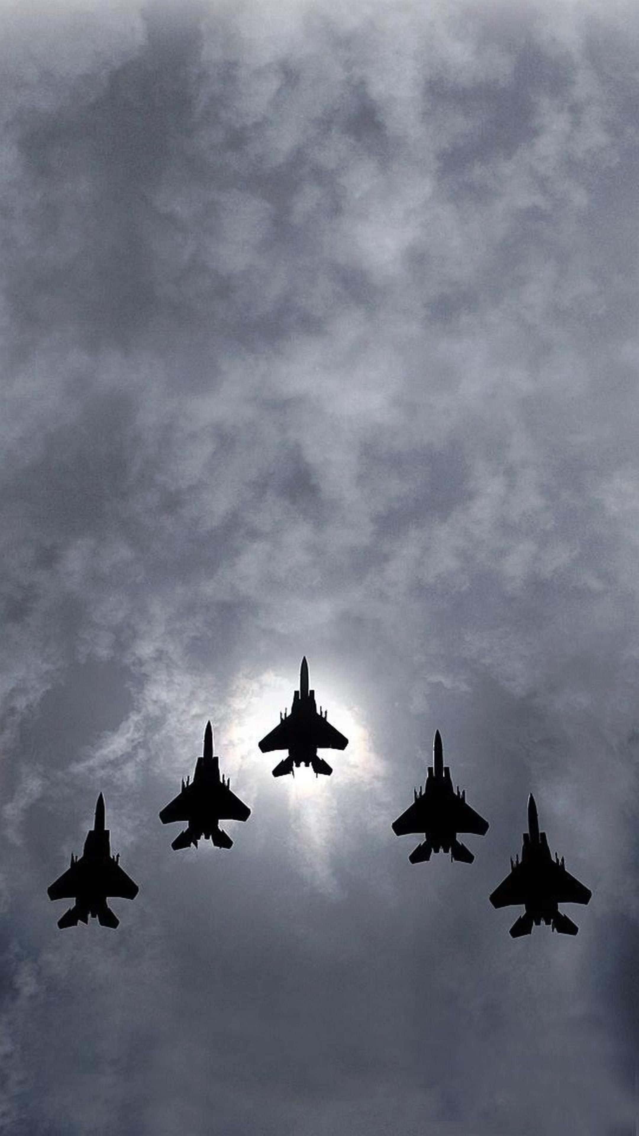 Military Plane 桌布 壁紙 — 五架戰鬥機在戲劇性的多雲天空下緊密編隊飛行，太陽在它們身後明亮地照耀。