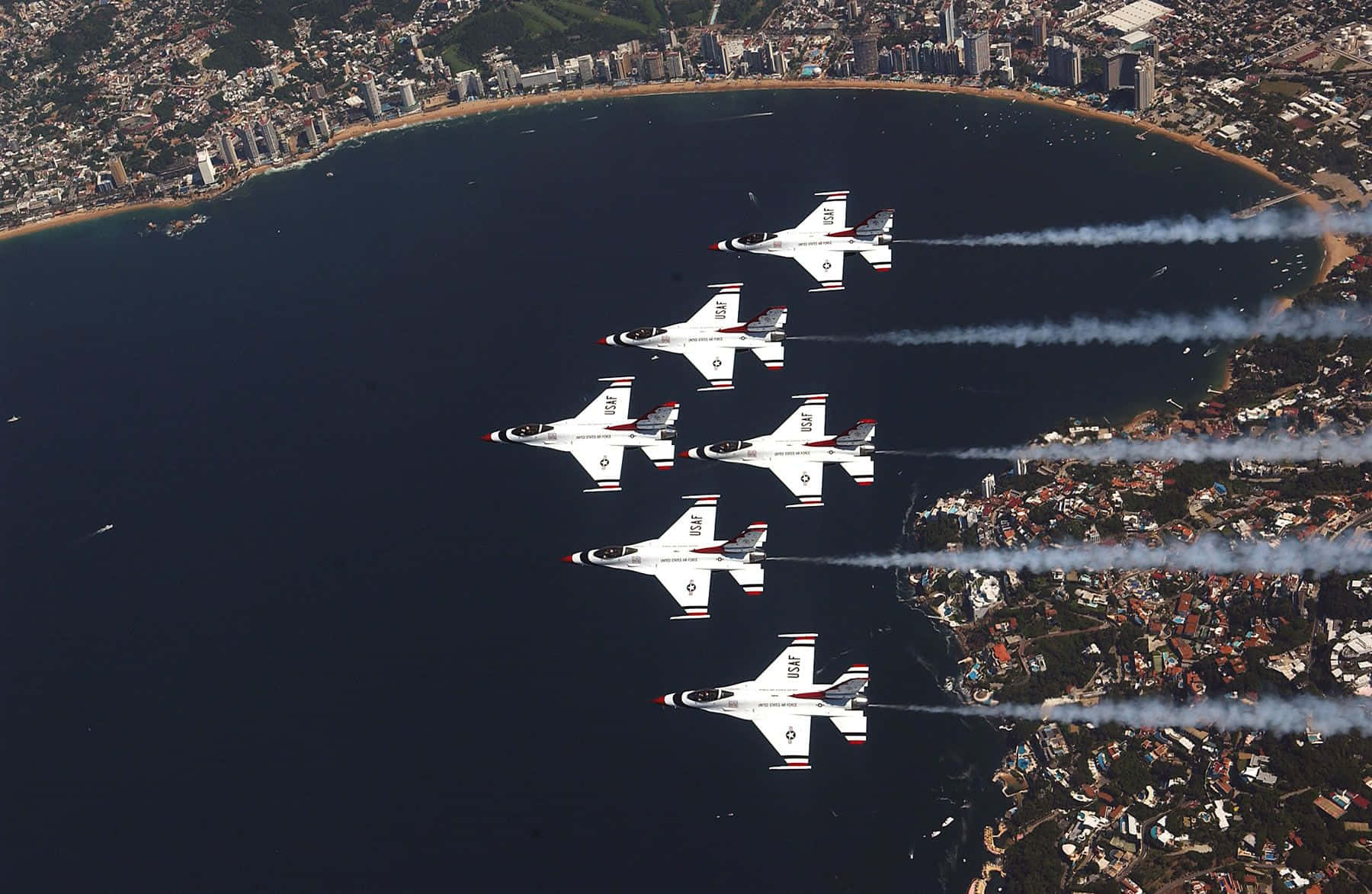 Air Force 桌布 壁紙 — 五架白色戰鬥機以緊密編隊飛越沿海城市，在深藍色海水上空留下煙跡。