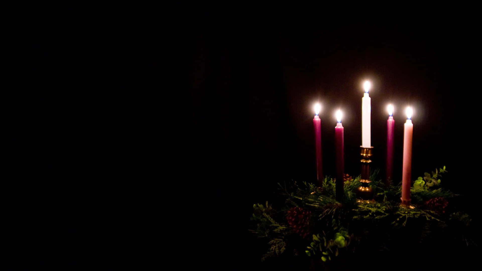 Advent 桌布 壁紙 — 五根點燃的蠟燭在金色燭台中溫暖地發光，背景是漆黑的，周圍環繞著常綠的樹葉。