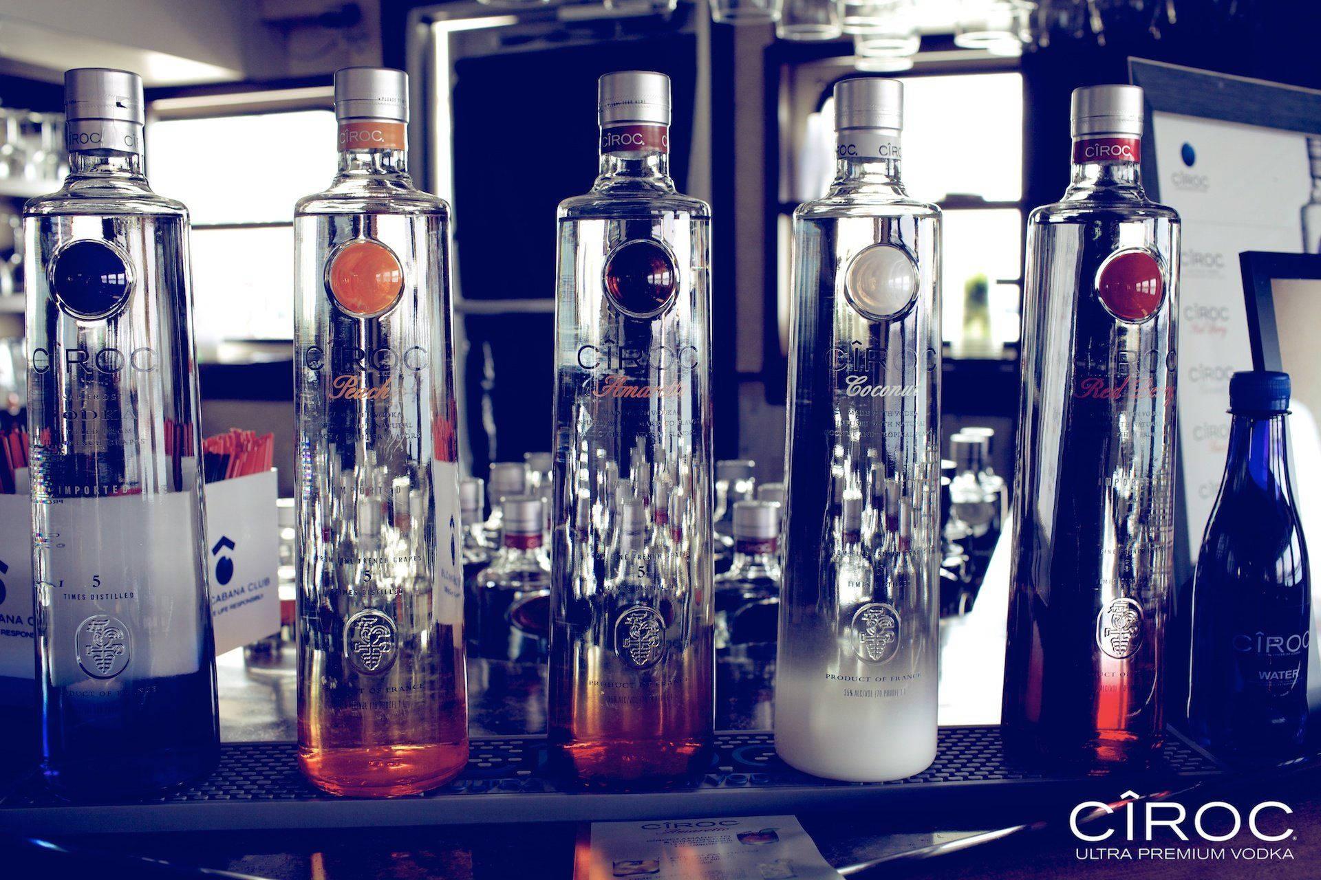 Drink 桌布 壁紙 — 五款不同口味的Ciroc伏特加酒瓶整齊排列在酒吧架上，反射環境光線，背景模糊。