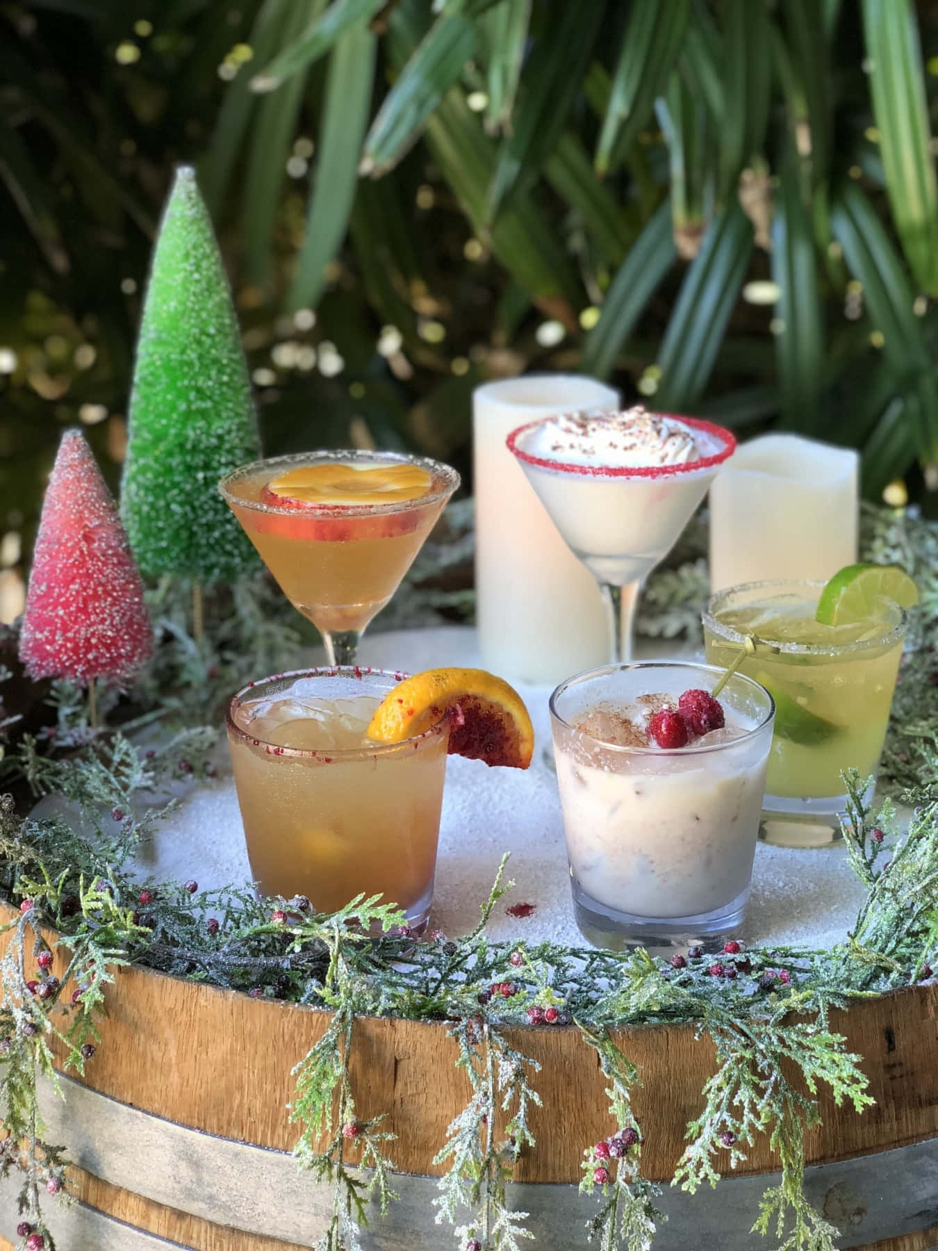 Winter Drinks 桌布 壁紙 — 五款節日雞尾酒，飾以水果和莓果，放在一個覆雪的桶上，桶上裝飾著糖霜小樹和常綠花環。