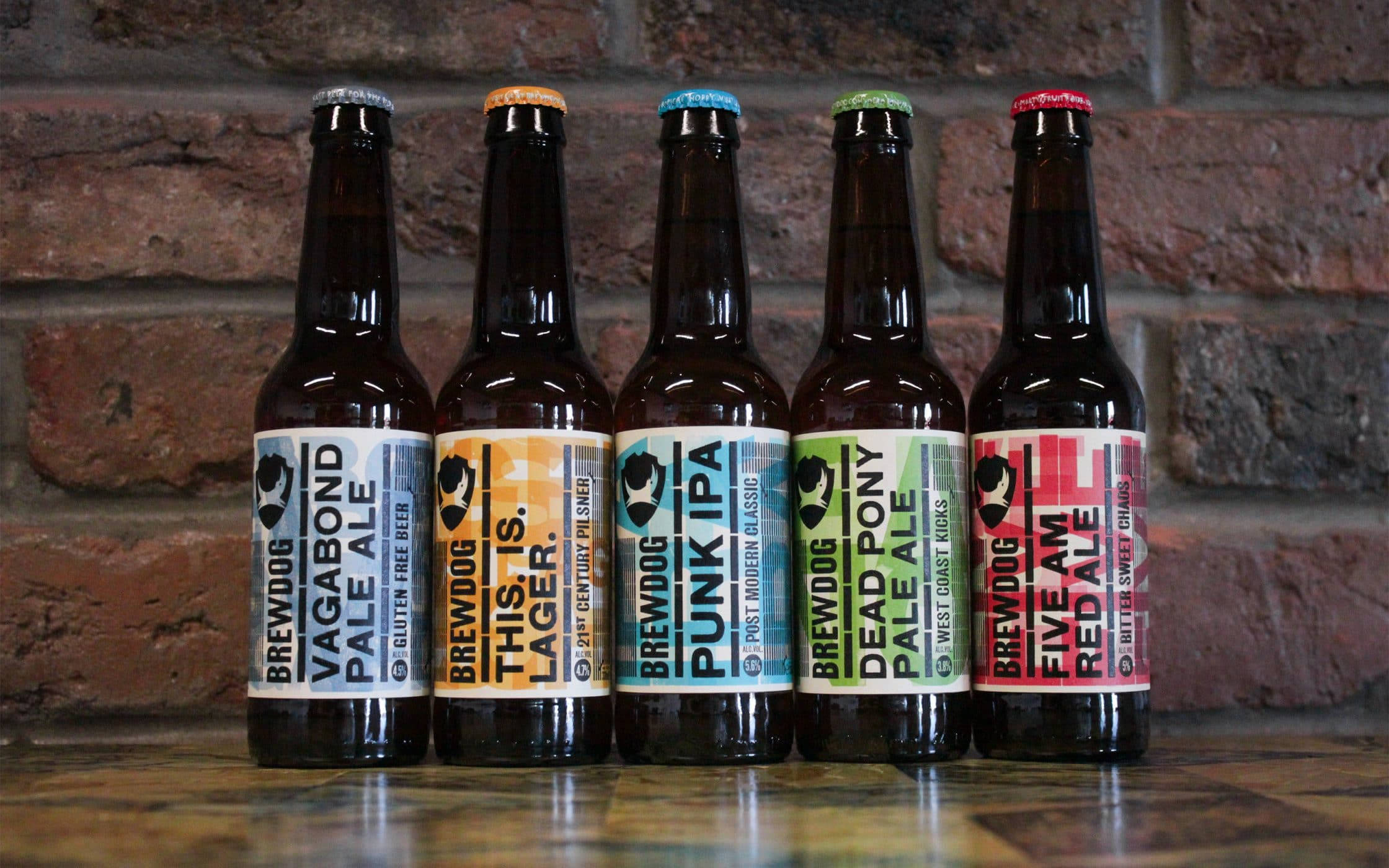 Drink 桌布 壁紙 — 五款色彩繽紛的BrewDog啤酒瓶排列在木質表面上，背景是質樸的磚牆。