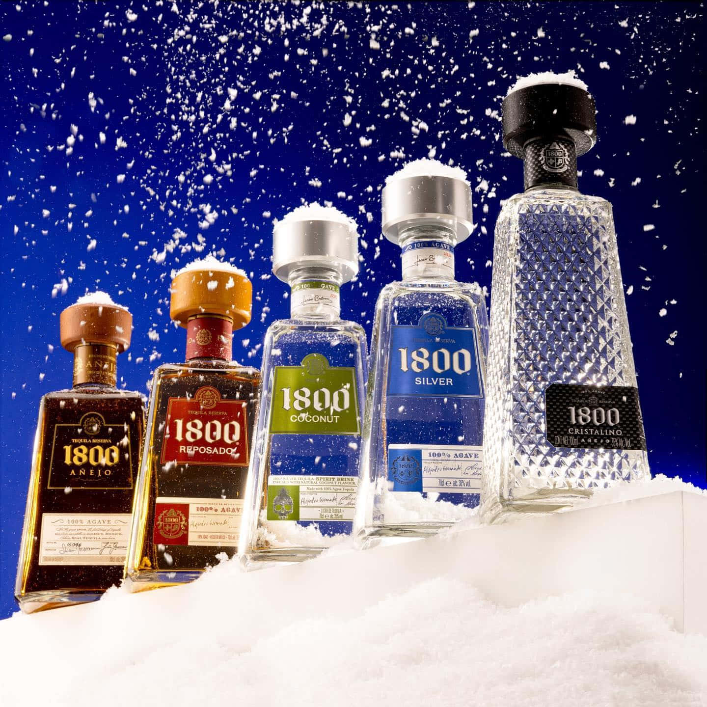 alcohol 桌布 壁紙 — 五瓶1800龍舌蘭酒矗立在新雪中，背景是深藍色的天空和飄落的雪花。