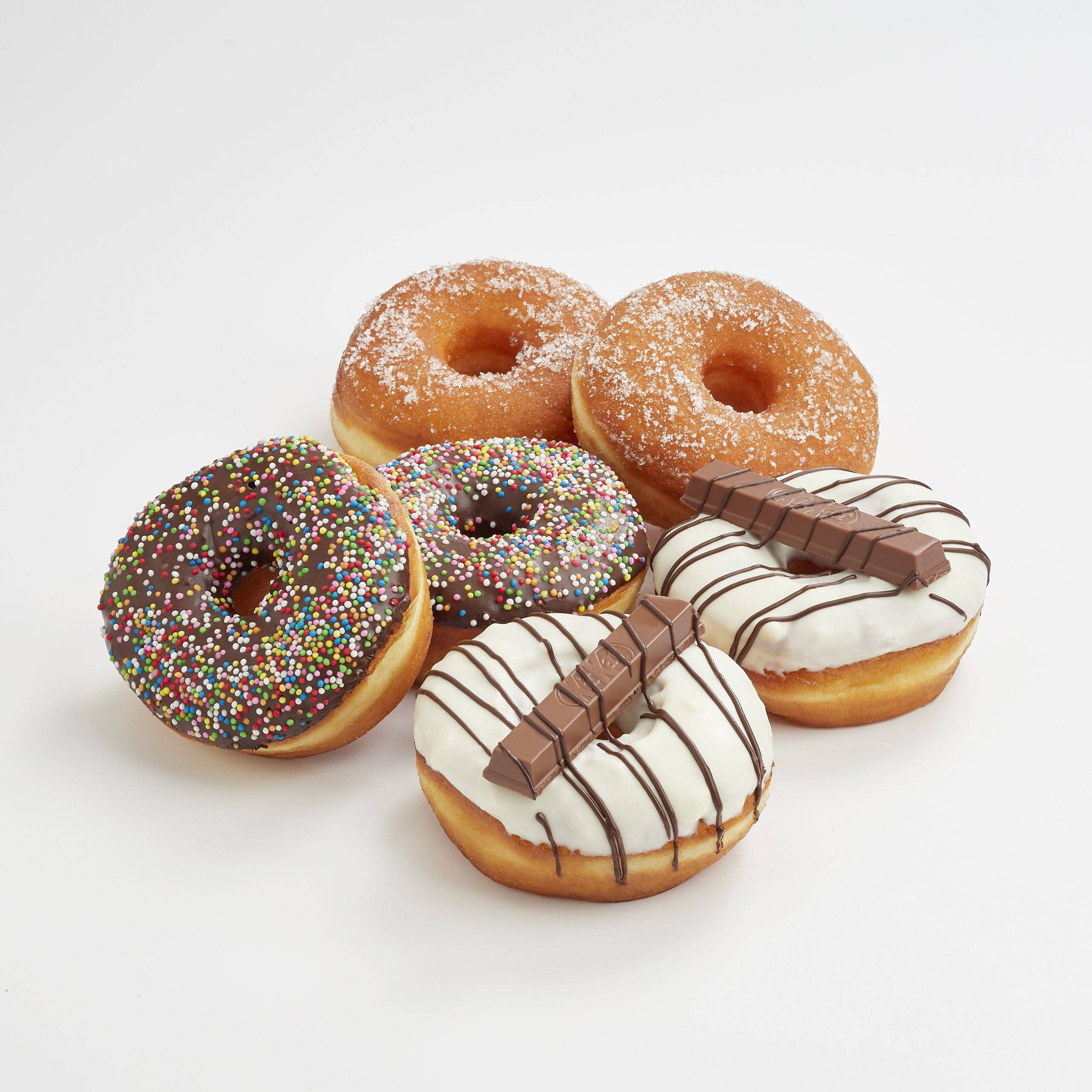 Donut 桌布 壁紙 — 五種不同的甜甜圈，搭配巧克力碎、白色糖霜和巧克力棒，整齊排列在潔白的表面上。