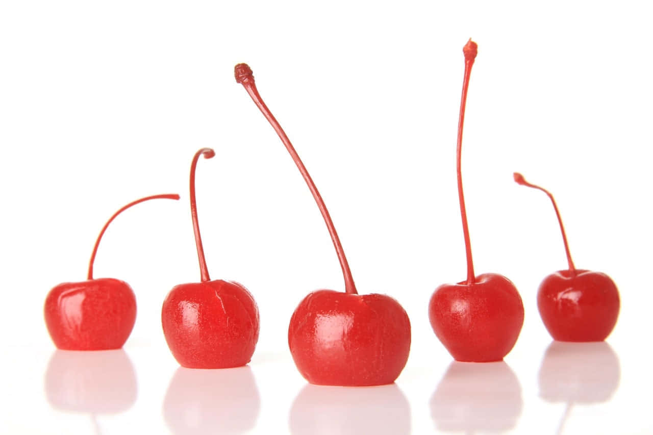 Red Cherries 桌布 壁紙 — 五顆帶莖的光亮紅櫻桃排成一列，置於白色反光表面上。