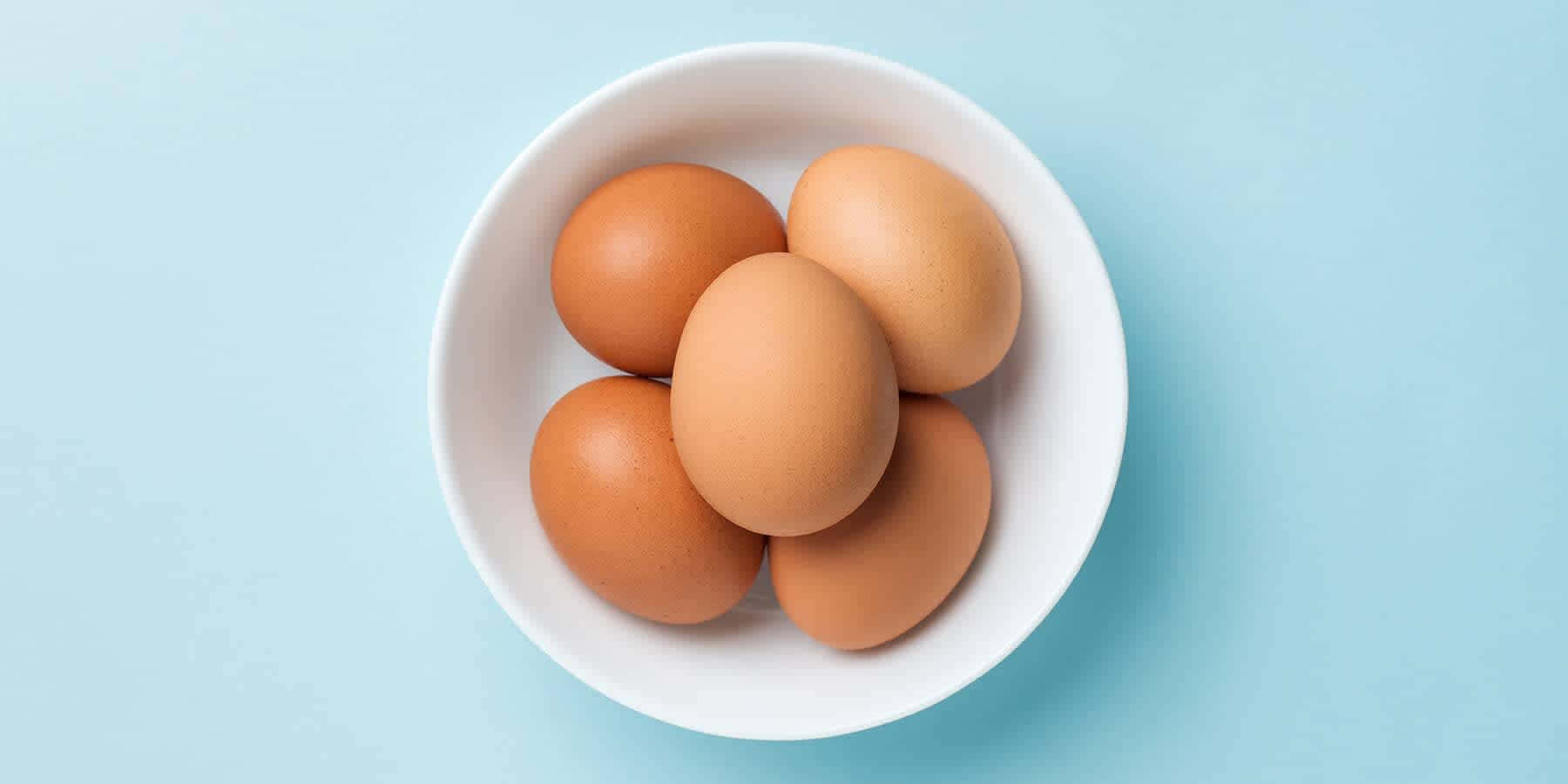 Egg 桌布 壁紙 — 五顆棕色雞蛋放在一個白色碗裡，襯著柔和的藍色背景。