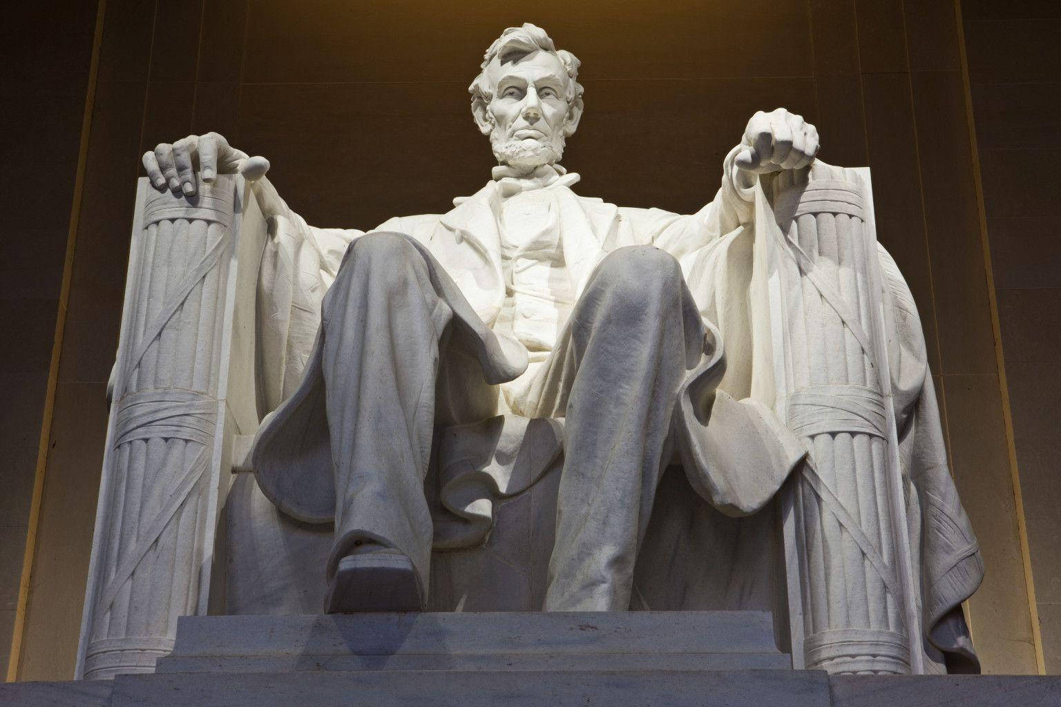 Lincoln Monument 桌布 壁紙 — 亞伯拉罕·林肯的大型大理石雕像，以莊嚴姿態坐在光線昏暗的大廳內，雙手擱在柱子上。