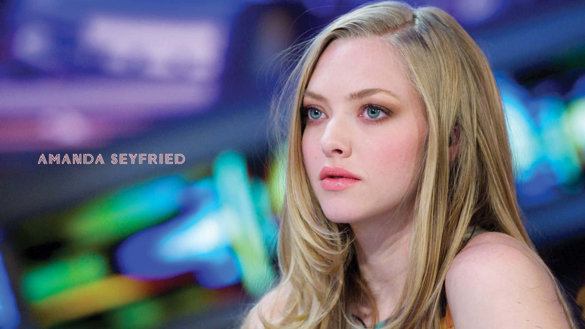 Amanda Seyfried 桌布 壁紙 — 亞曼達·塞佛瑞在充滿活力的模糊霓虹背景前沉思，背景帶有冷色調的藍色和綠色。