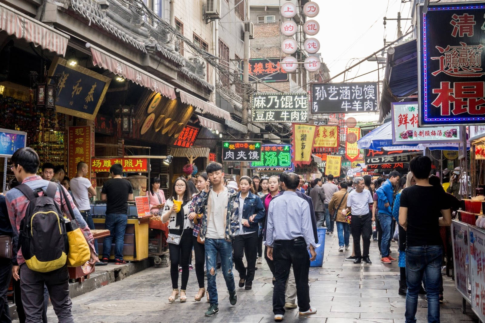 Xian 桌布 壁紙 — 亞洲城市中一條繁忙狹窄的街道，擠滿行人，頭頂懸掛著色彩繽紛的發光食物招牌。