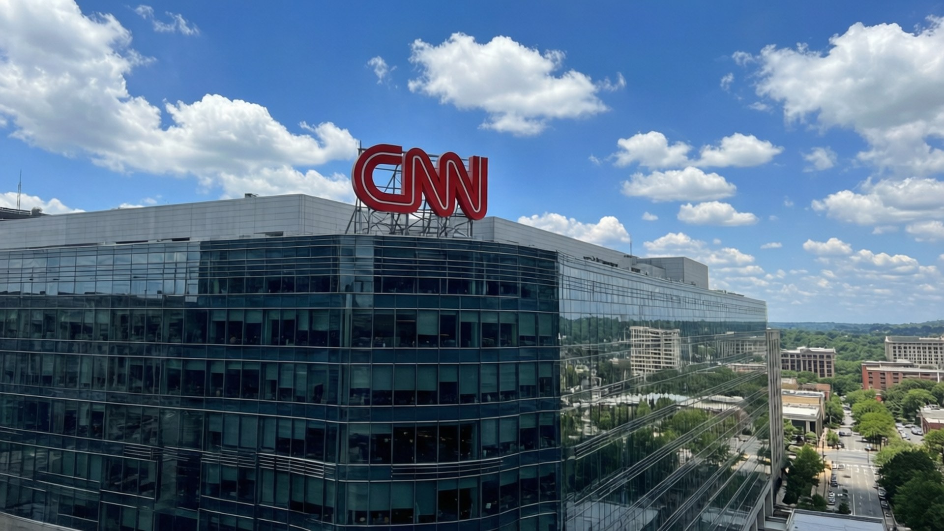 亞特蘭大CNN總部 壁紙 — 一座現代玻璃摩天大樓，頂部有巨大的紅色CNN標誌，背景是明亮的藍天和蓬鬆的白雲。