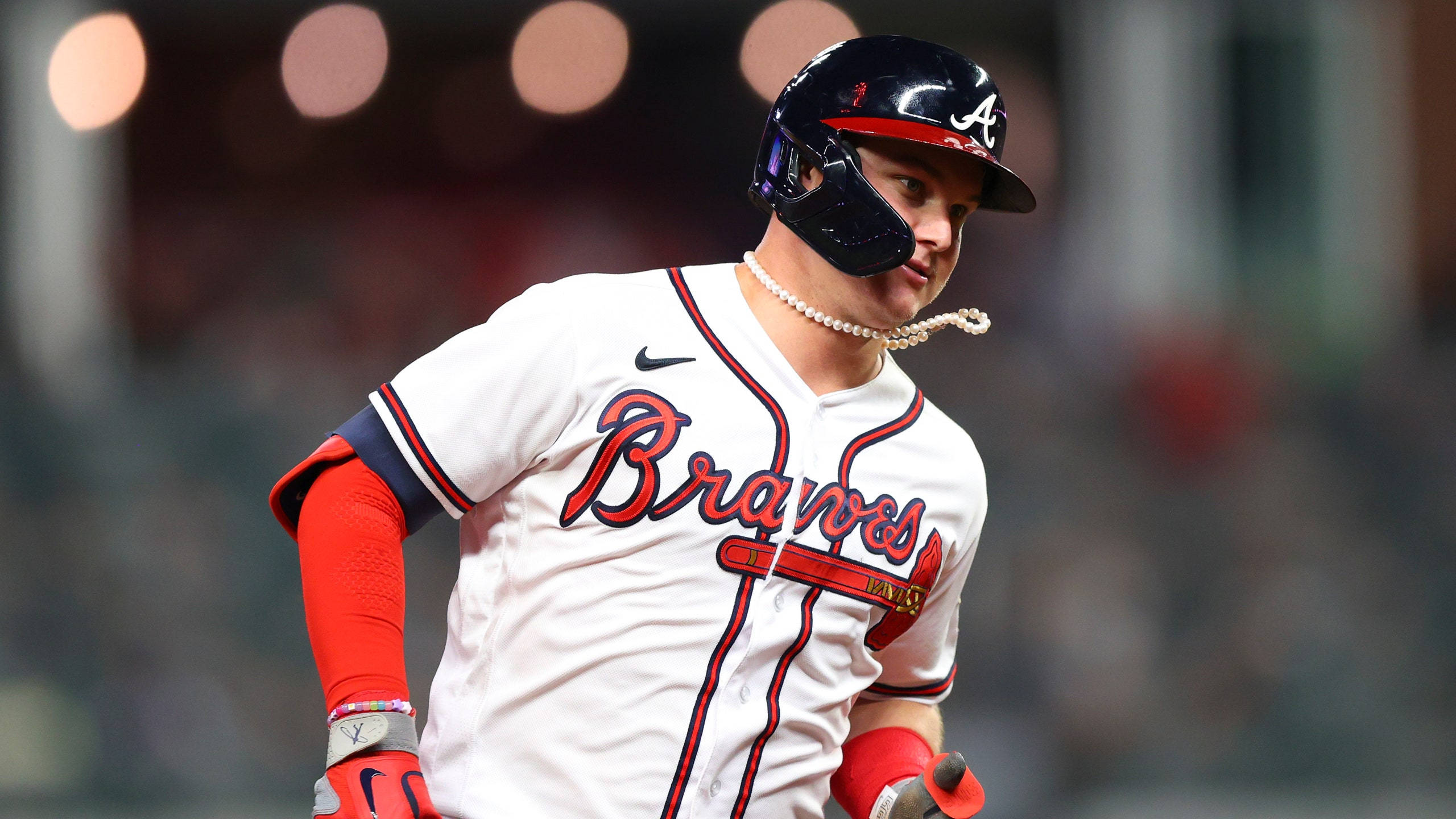 Braves 桌布 壁紙 — 亞特蘭大勇士棒球選手身穿白色球衣配紅色飾邊和黑色頭盔，在球場燈光下自信地走進球場。