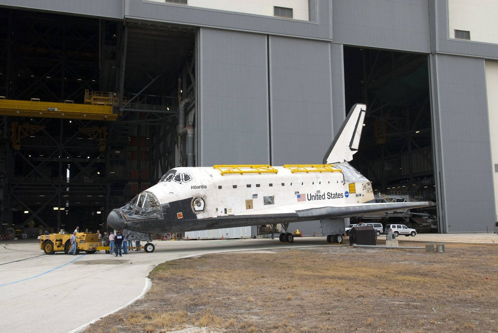 Nasa 桌布 壁紙 — 亞特蘭蒂斯號太空梭在一個大型機庫外展示，附近有工人和車輛。