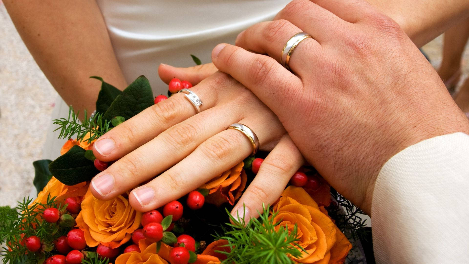 Wedding Rings 桌布 壁紙 — 交織的結婚戒指放在一束鮮豔的橙色玫瑰和紅色漿果上。