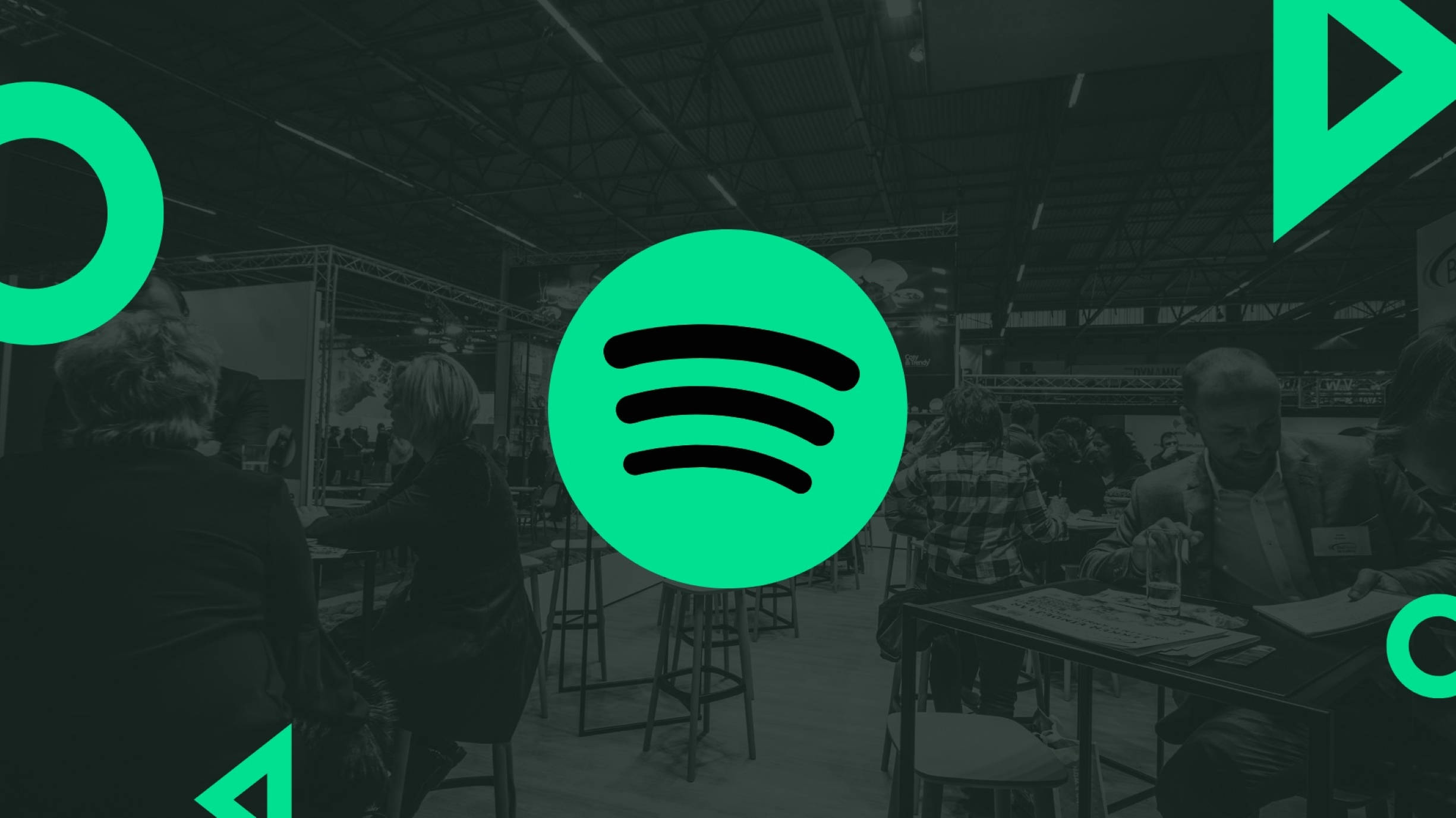 Spotify 桌布 壁紙 — 亮綠色的Spotify標誌主導了一個燈光昏暗的會議廳，有參加者在攤位。