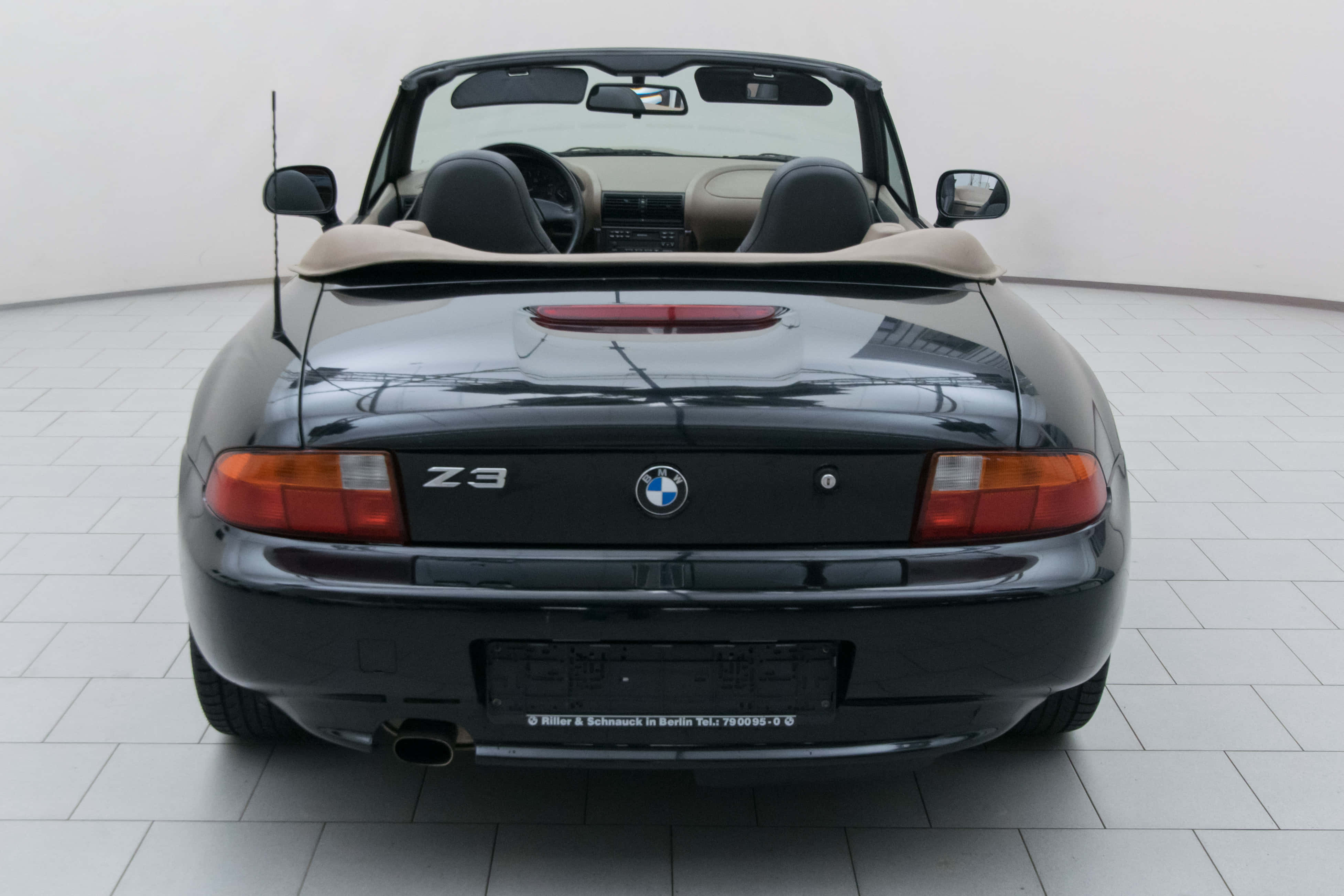 Bmw Z3 桌布 壁紙 — 亮黑色BMW Z3敞篷車配米色內裝，停放在明亮工作室的瓷磚地板上，從後方觀看。