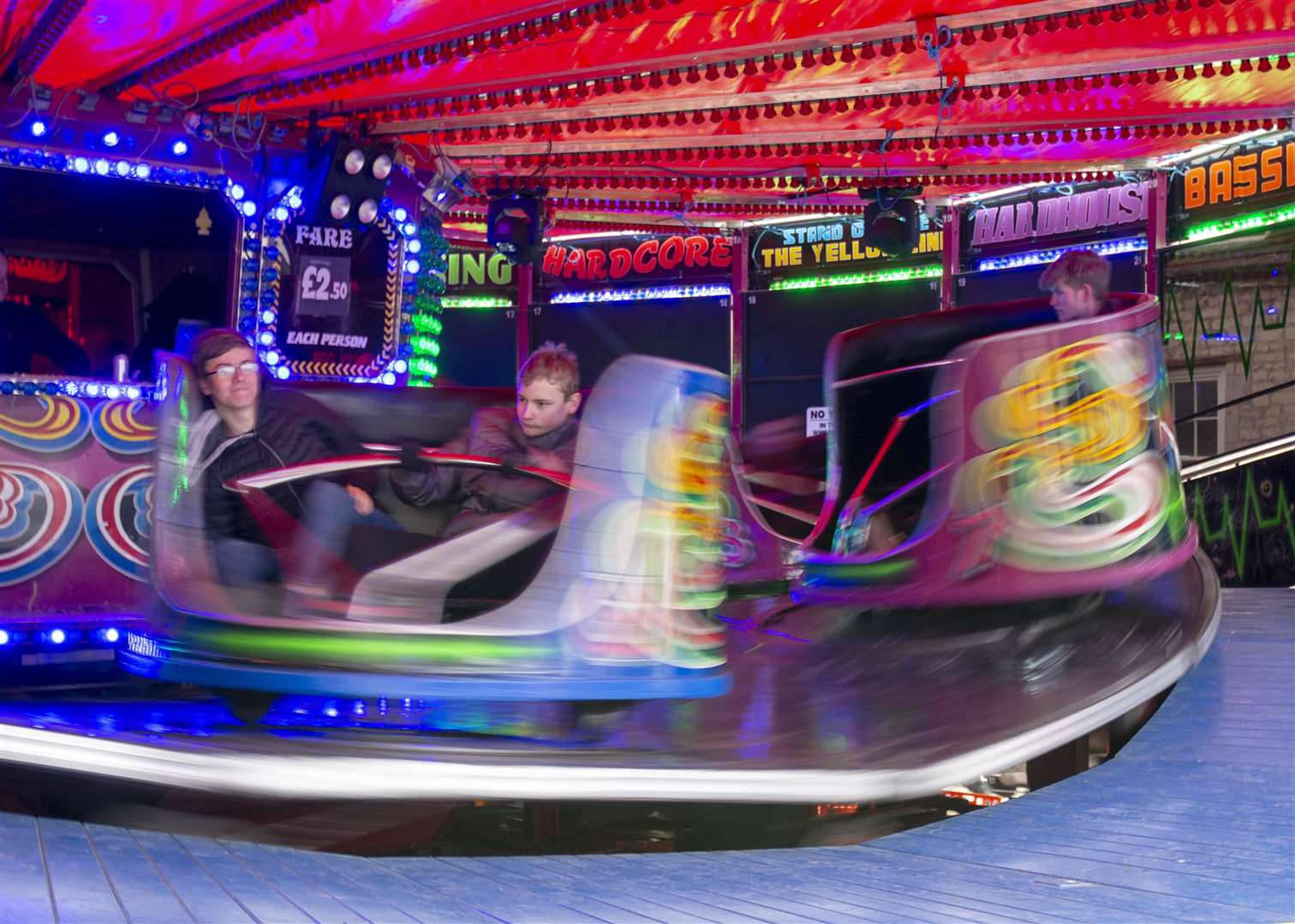 Roller Coaster 桌布 壁紙 — 人們乘坐旋轉的嘉年華遊樂設施，在充滿活力的天篷下，伴隨著色彩繽紛的燈光和動態模糊。