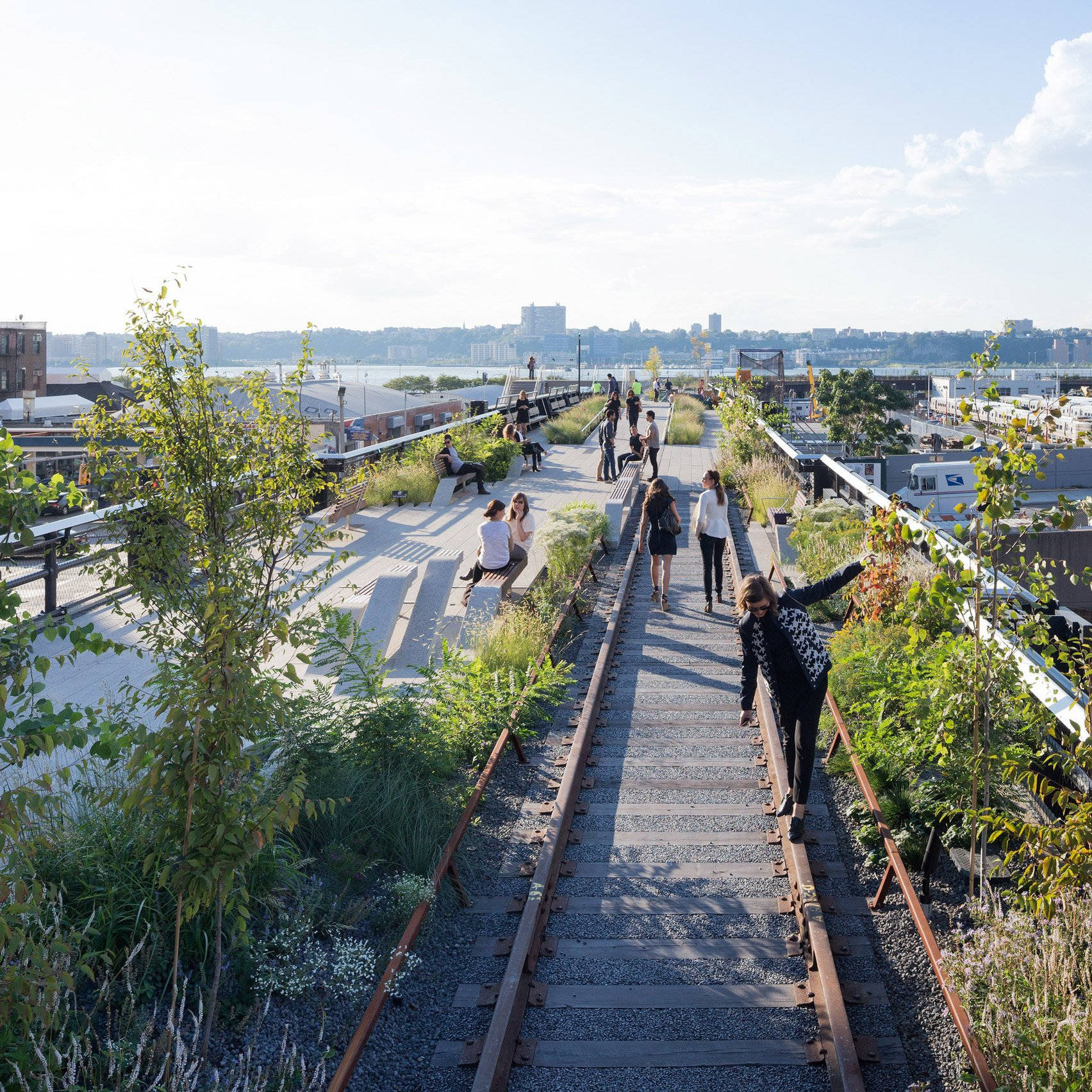 New York 桌布 壁紙 — 人們在一個陽光普照、建於改造火車軌道上的高架公園中漫步和放鬆，四周綠意盎然，可欣賞城市天際線。