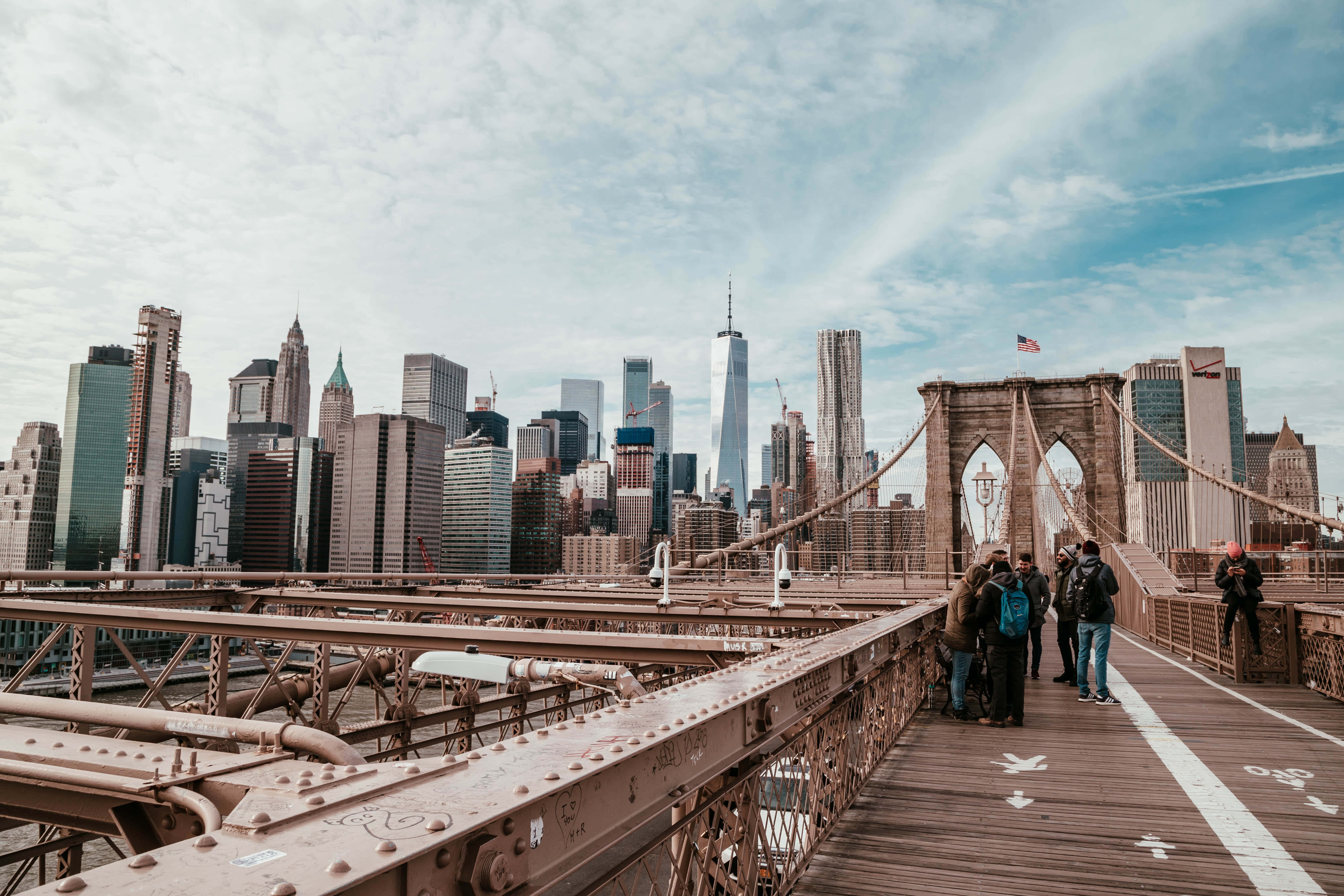 Nyc 桌布 壁紙 — 人們在布魯克林大橋上漫步，天空部分多雲，背景是標誌性的曼哈頓天際線。
